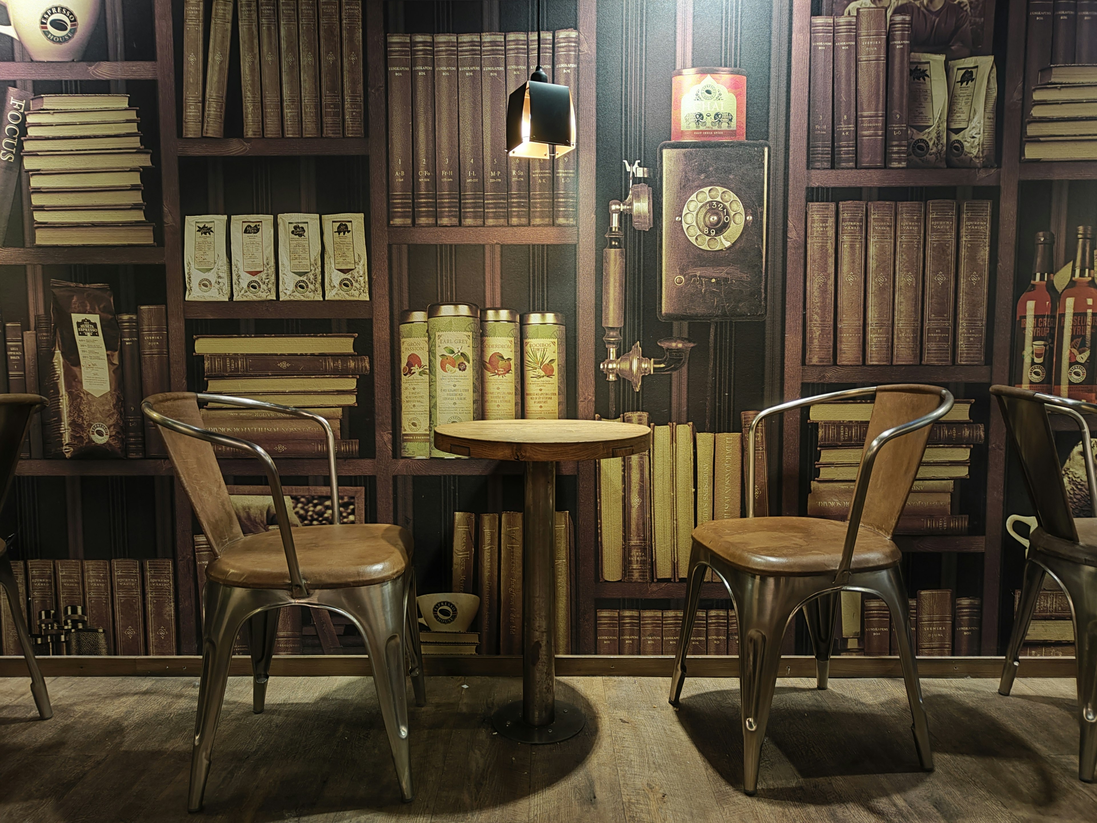 A cozy cafe corner with a wooden table and two chairs surrounded by a bookshelf filled with books