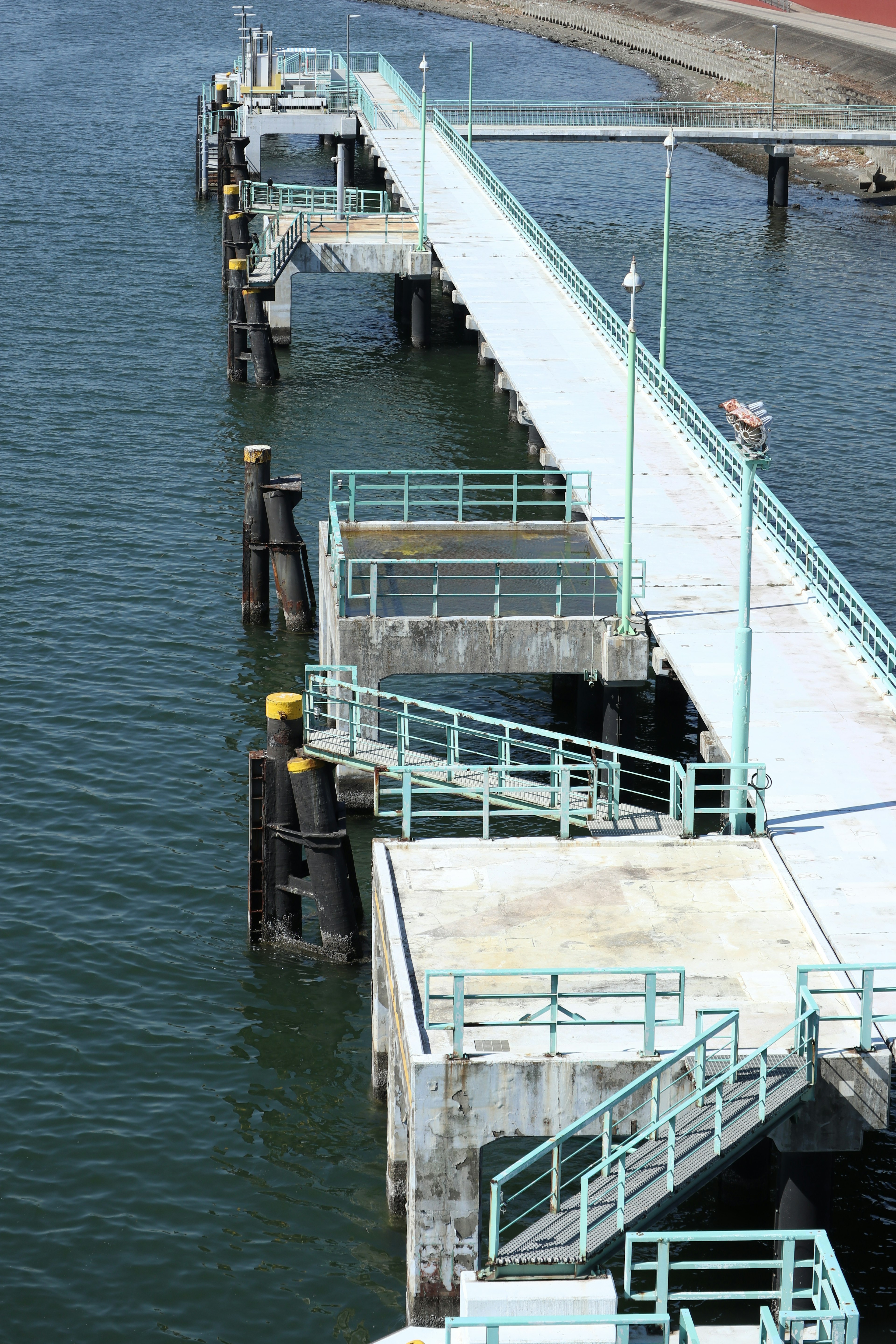 Image of a long pier by the water featuring blue railings and a concrete base