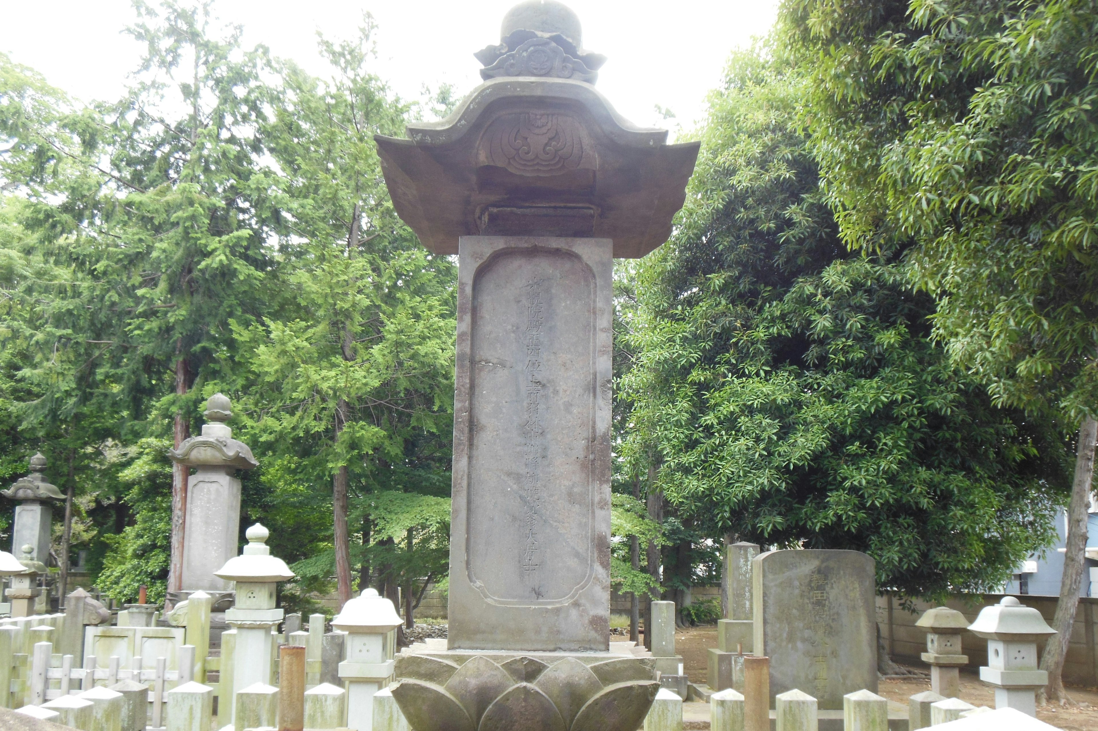 Stone lantern in a cemetery surrounded by gravestones with lush greenery