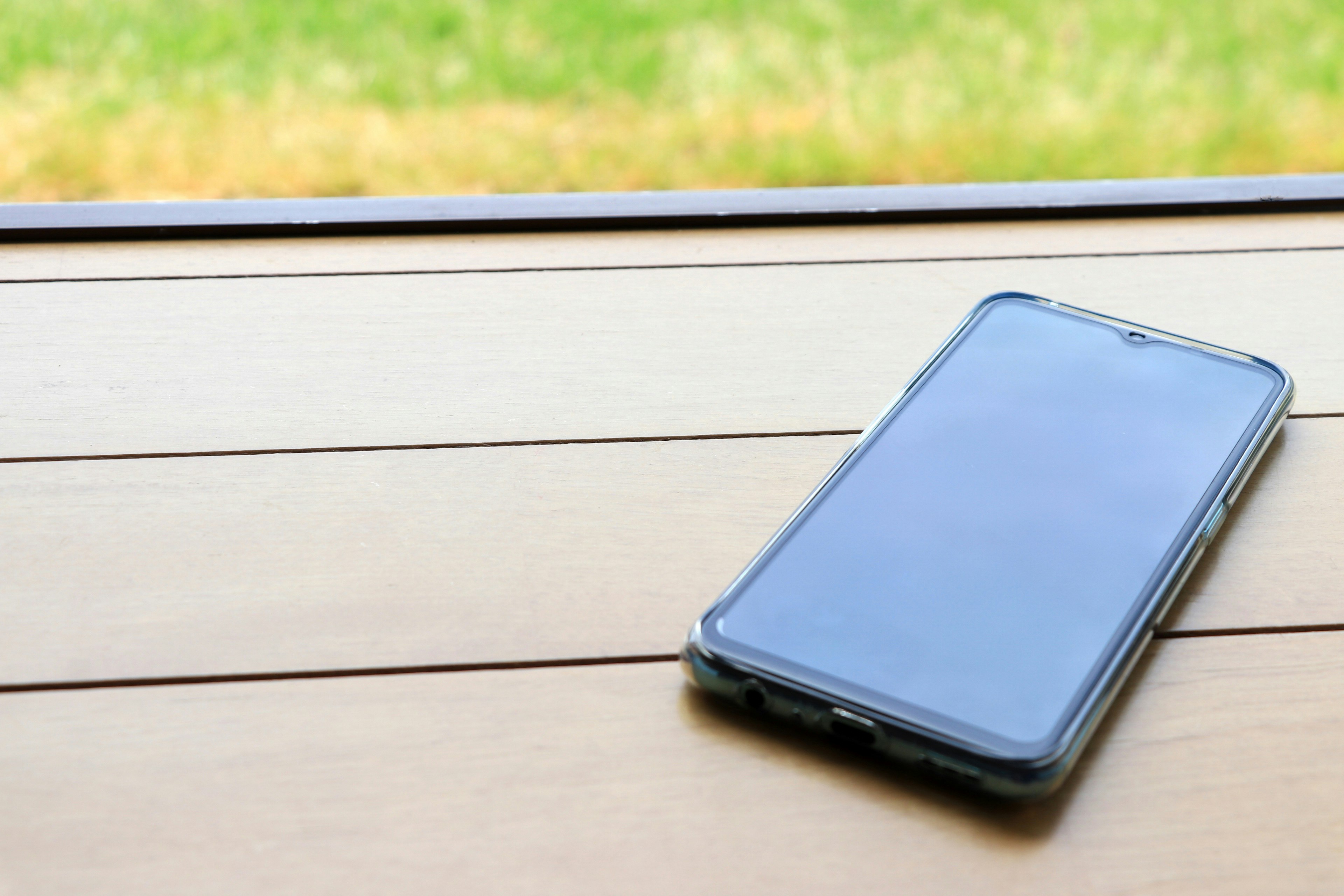 Smartphone resting on a wooden table with a green background