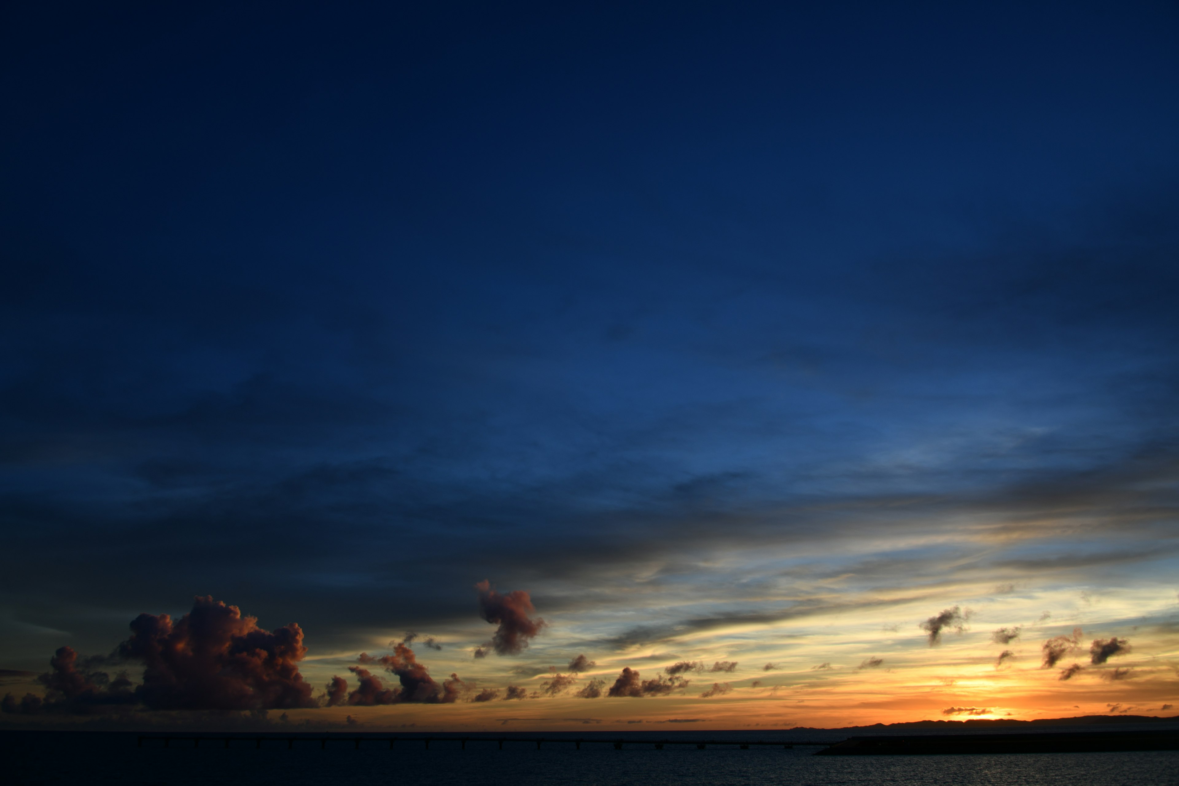 Sunset over the ocean with dark blue sky and orange clouds