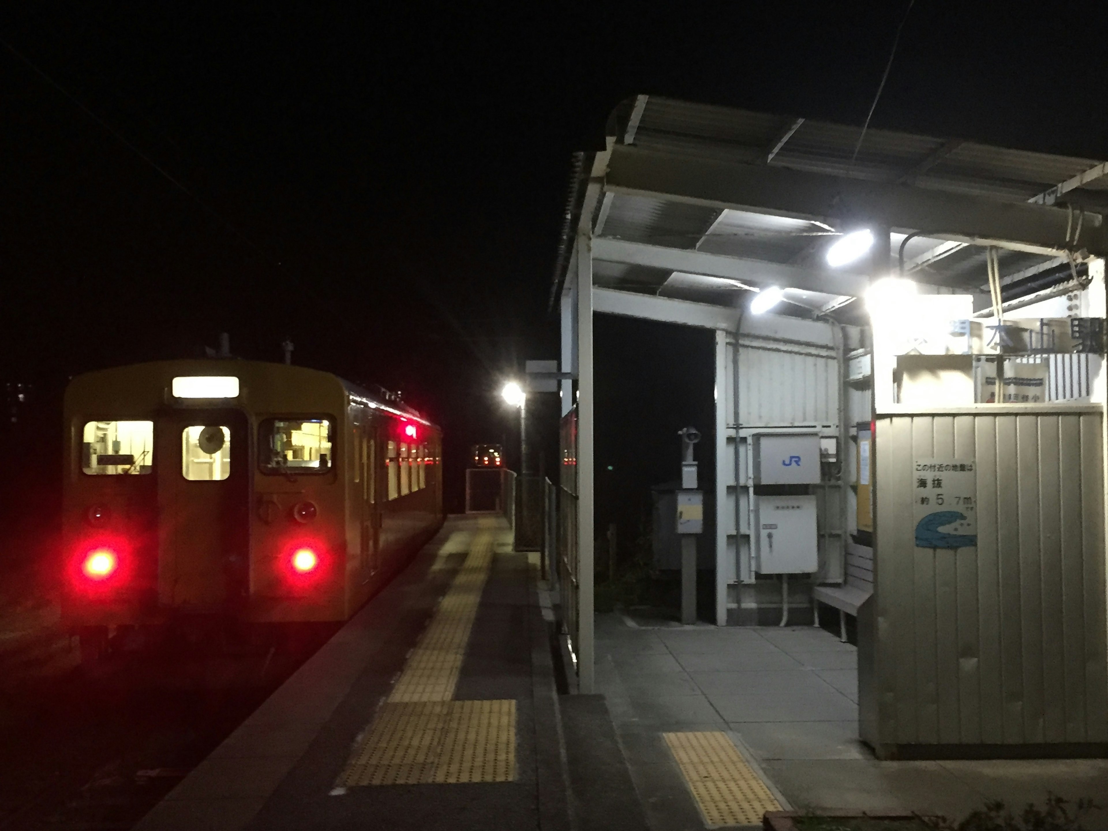 Zug, der nachts an einer Station hält, mit hellen Lichtern auf dem Bahnsteig