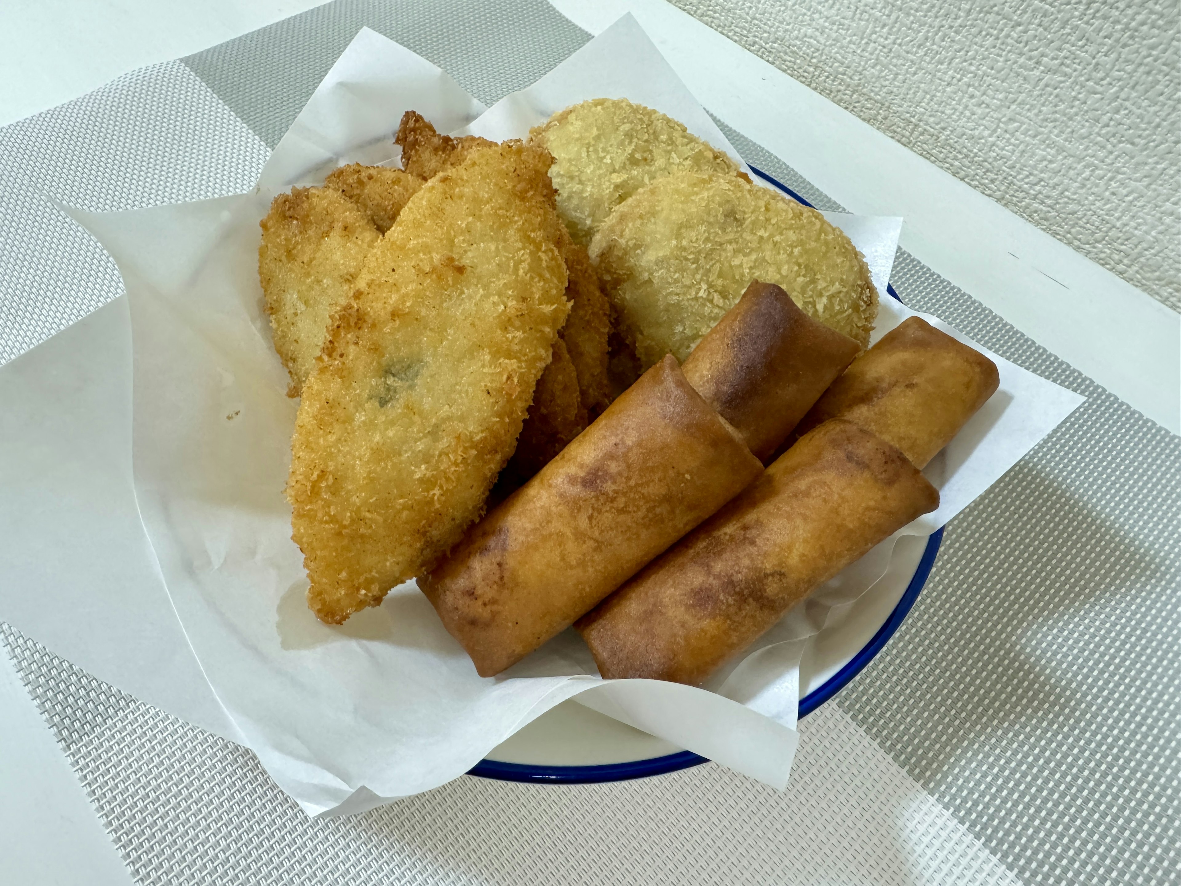 A platter of fried snacks including fish and spring rolls on a white plate