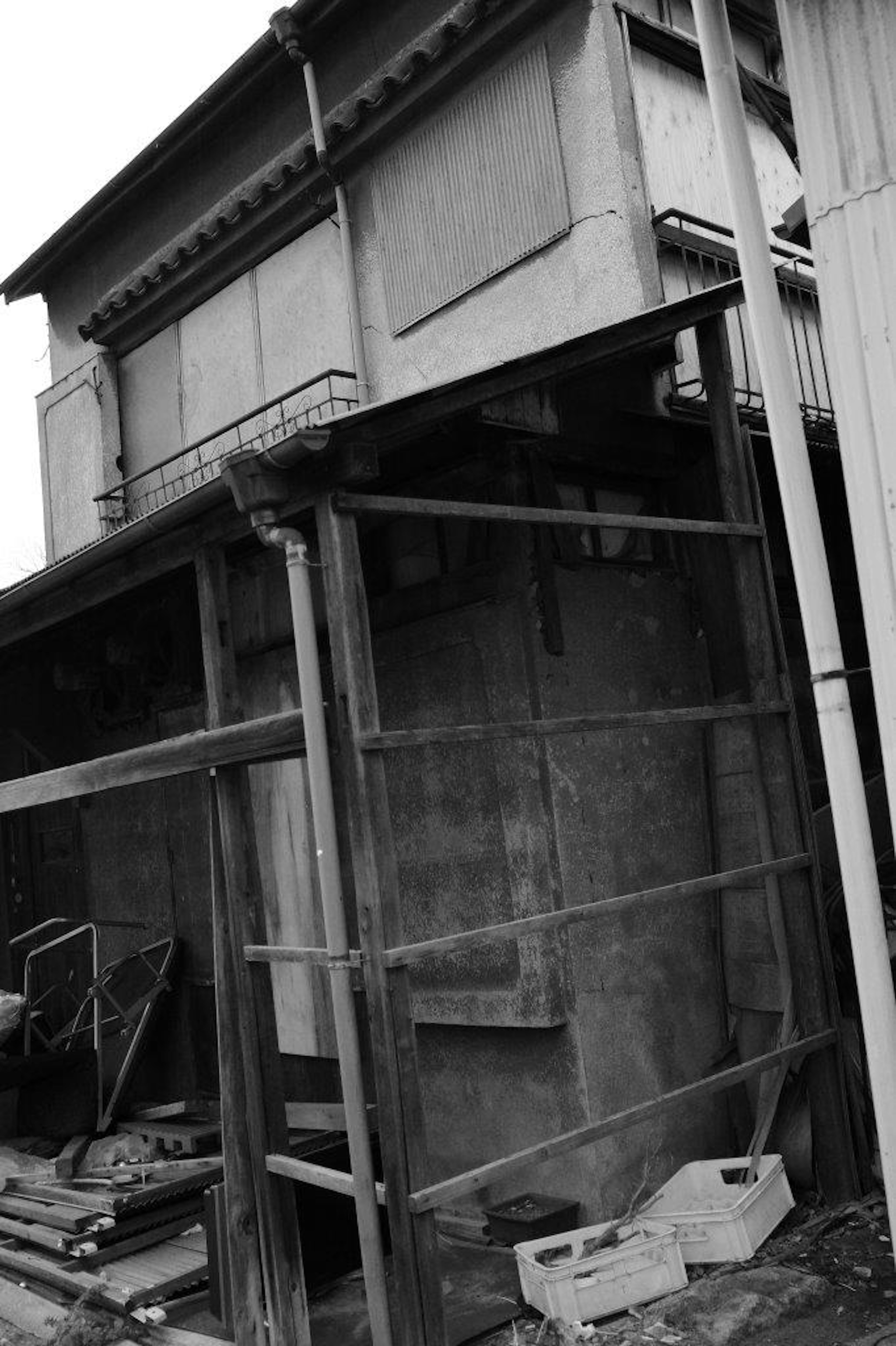 Photo en noir et blanc montrant le côté d'un vieux bâtiment avec des supports en bois et des matériaux éparpillés