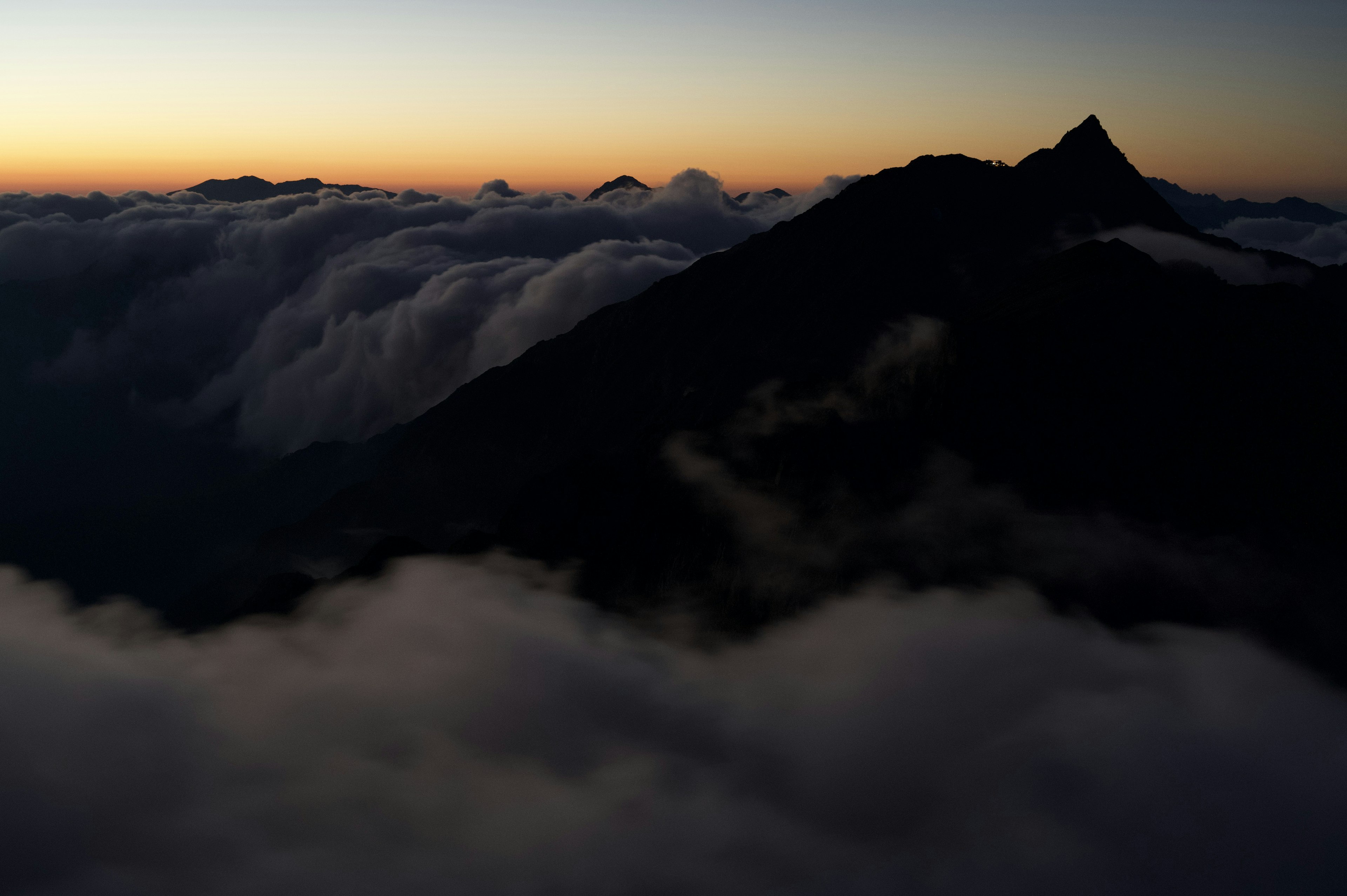 Silhouette of a mountain towering above the clouds at dawn