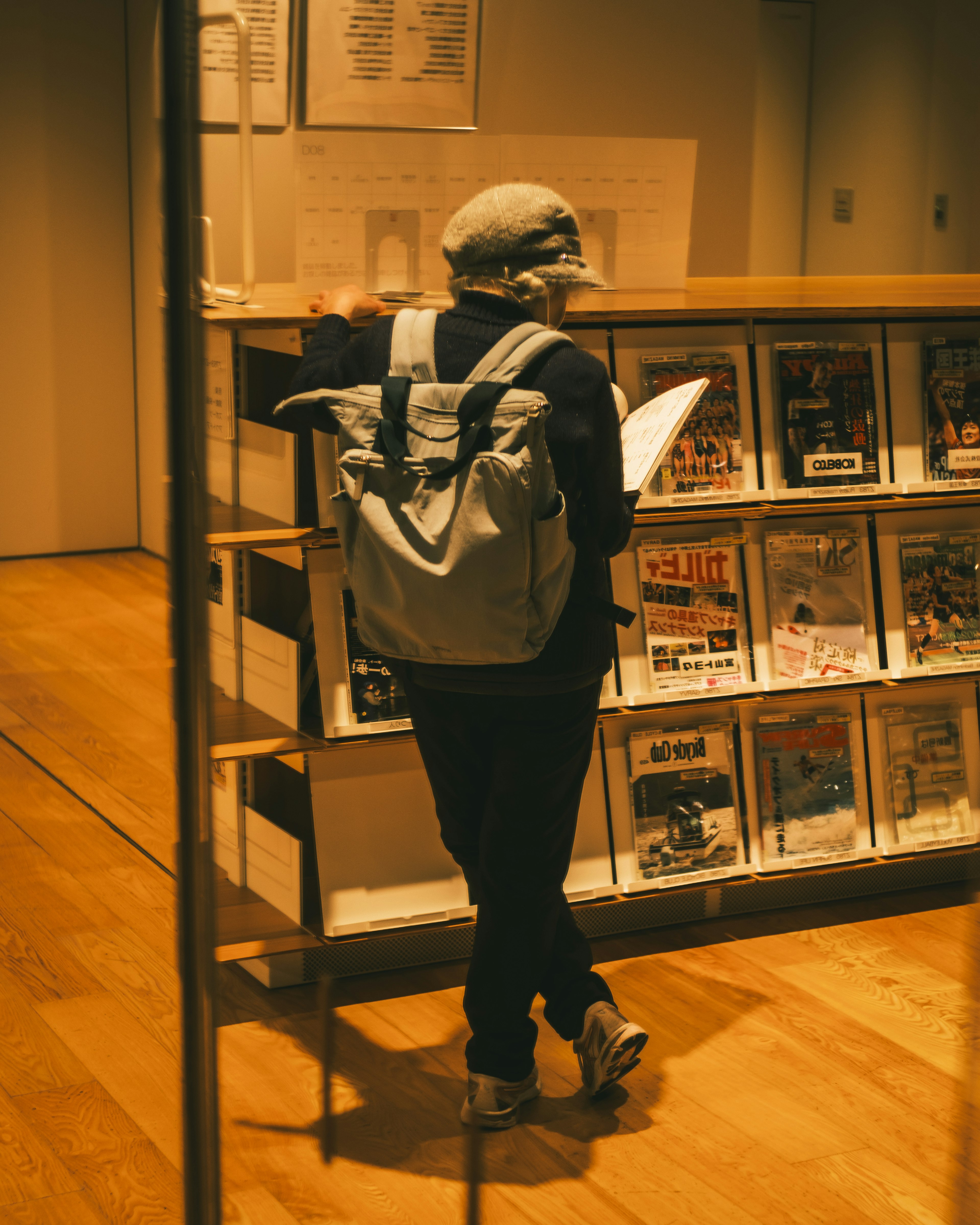 A person with a backpack reading magazines in a library interior