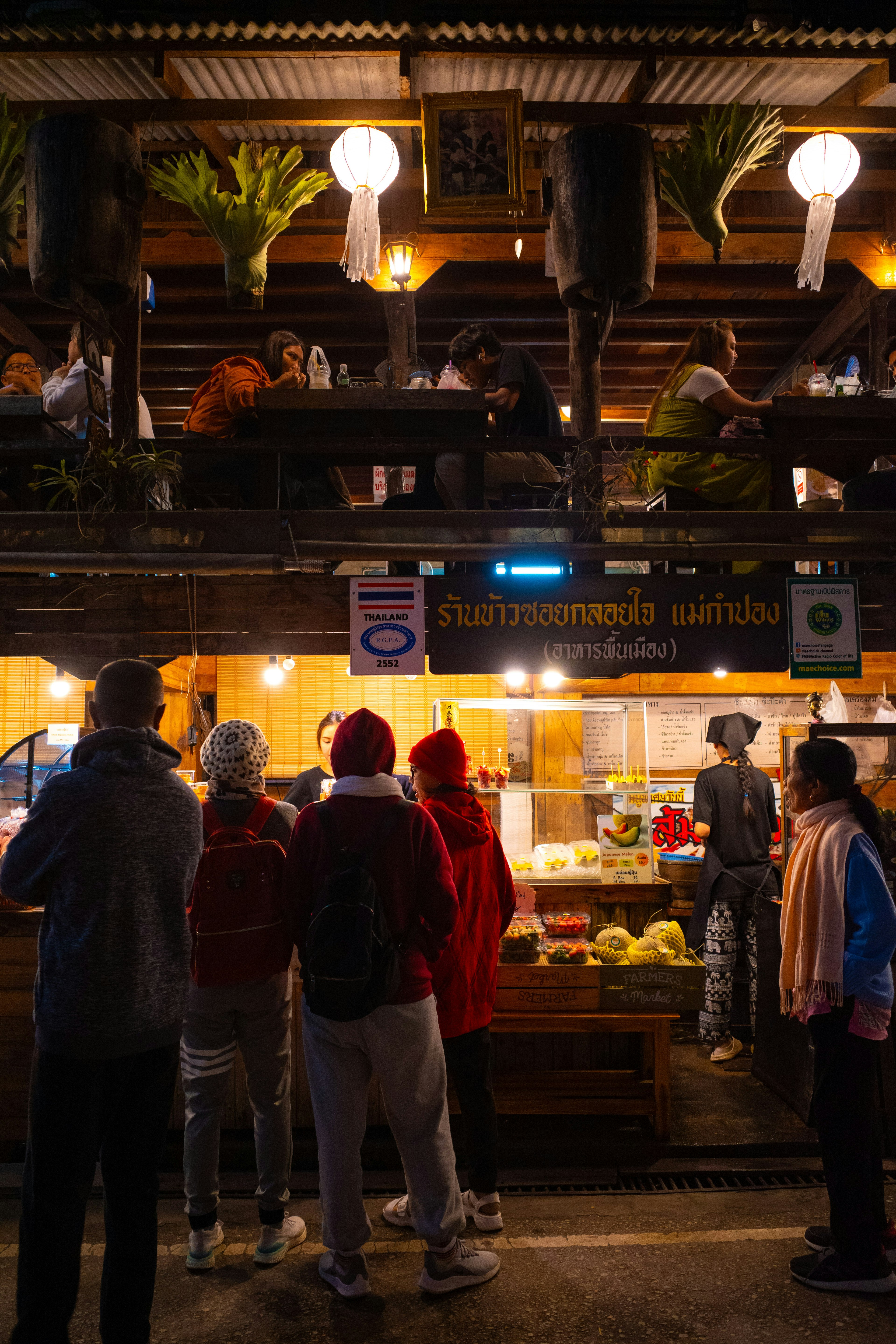 People gathered in front of a food stall under vibrant lighting