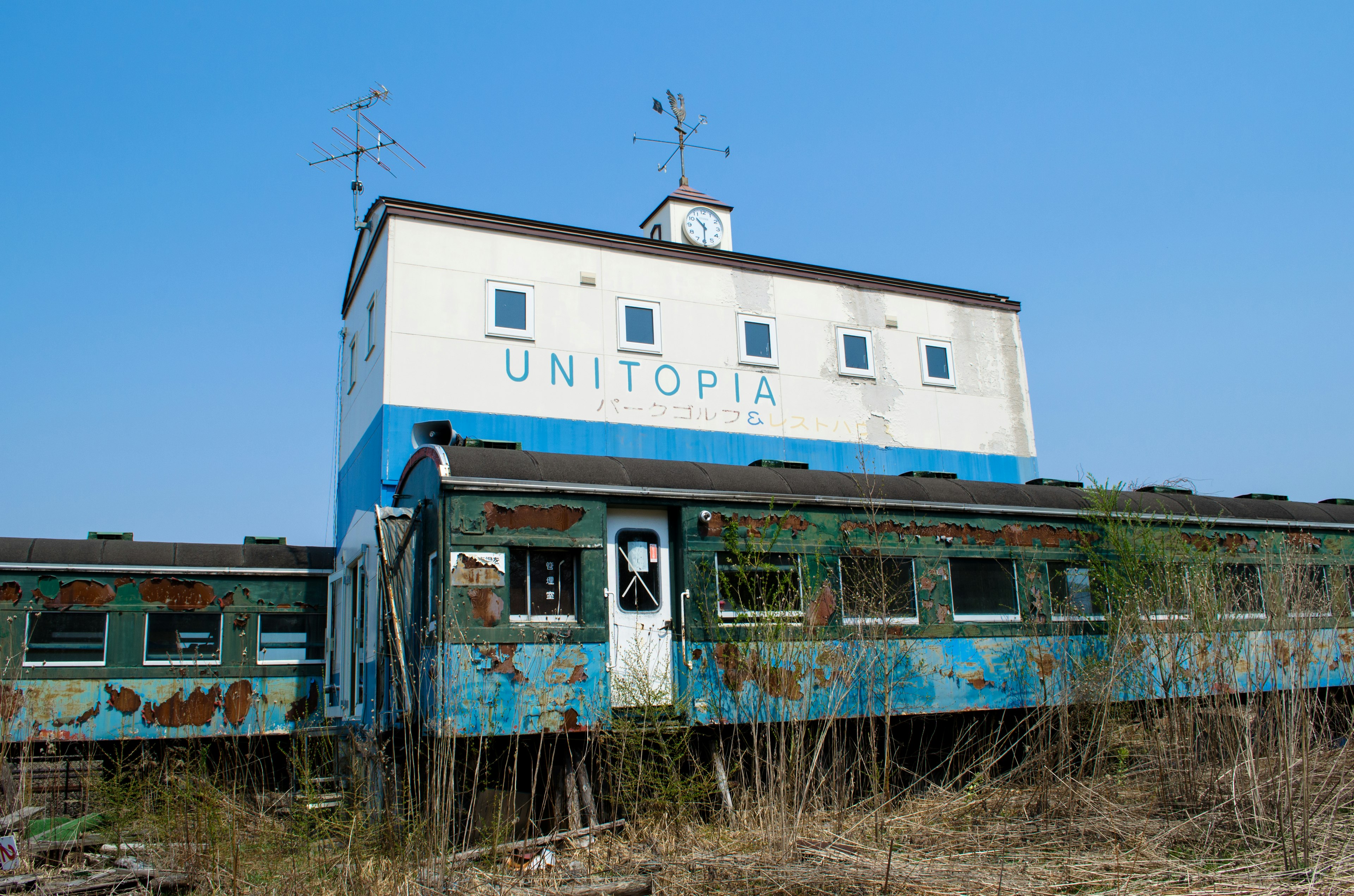 Edificio abbandonato con insegna 'UNITOPIA' blu e bianca accanto a carrozze di treno arrugginite