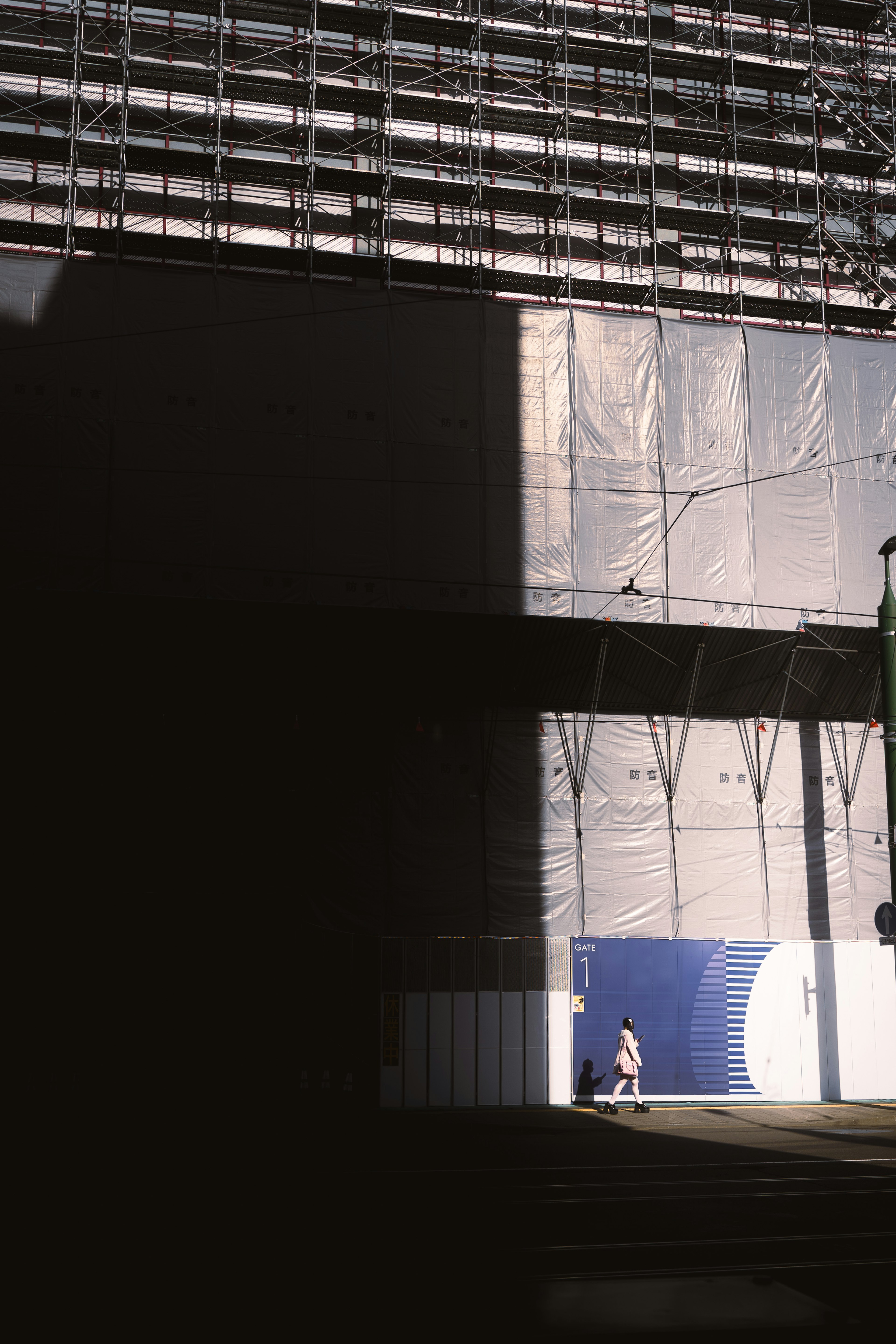 Contrasting shadows of a building under construction with a person walking in the foreground