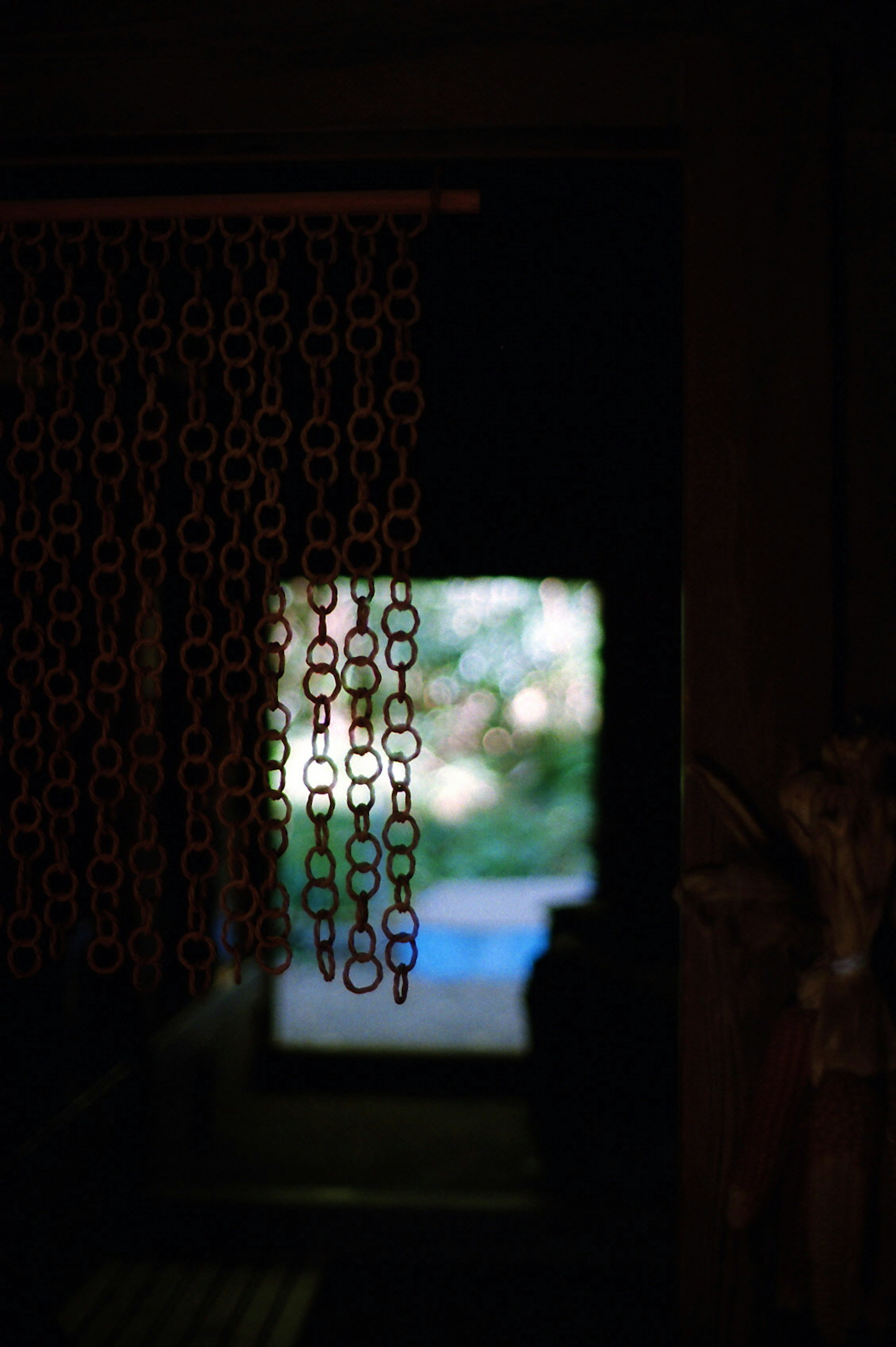 Cortina de cadenas en la entrada de una habitación oscura con vista a la vegetación exterior