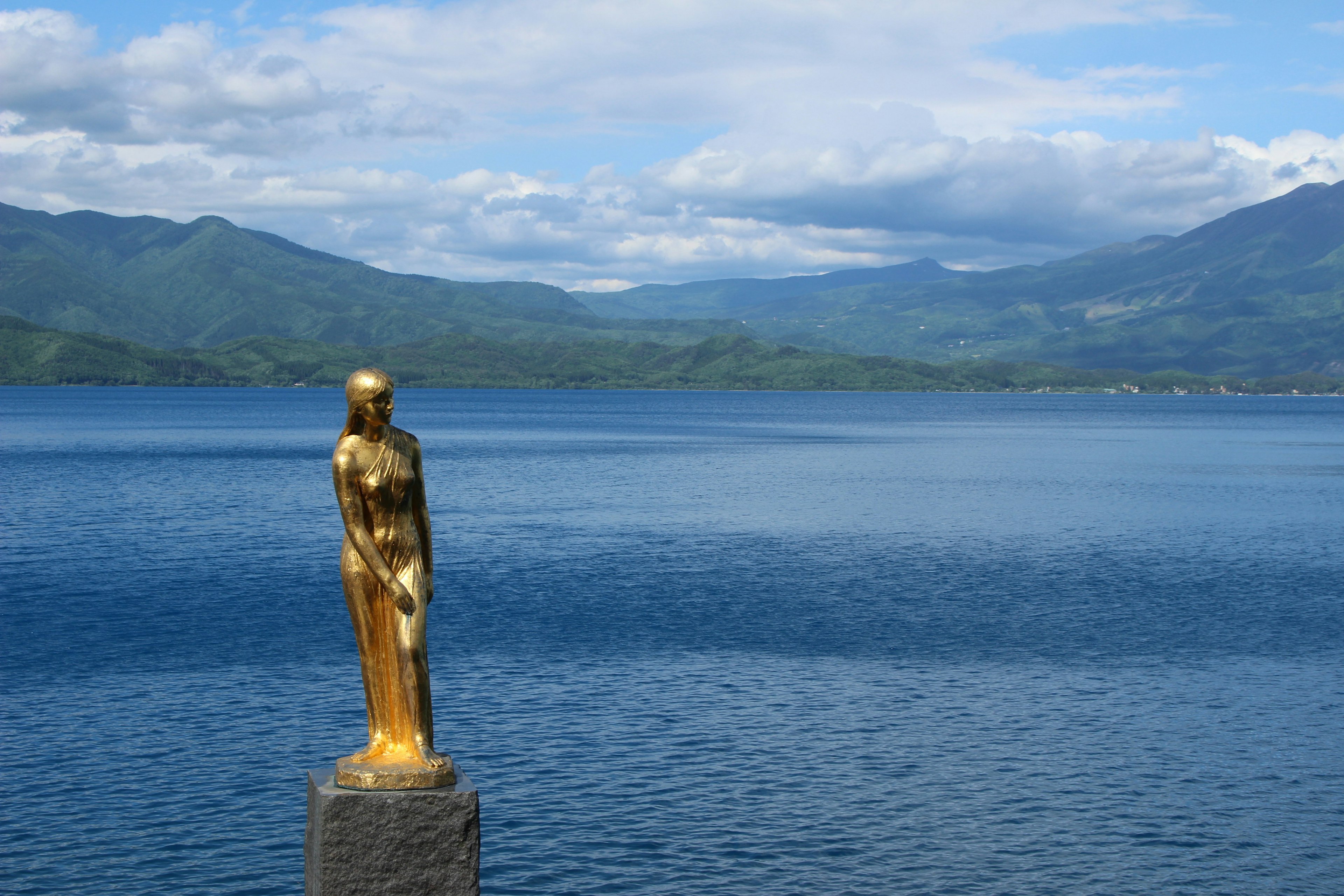 Estatua dorada de pie junto a un lago con montañas al fondo