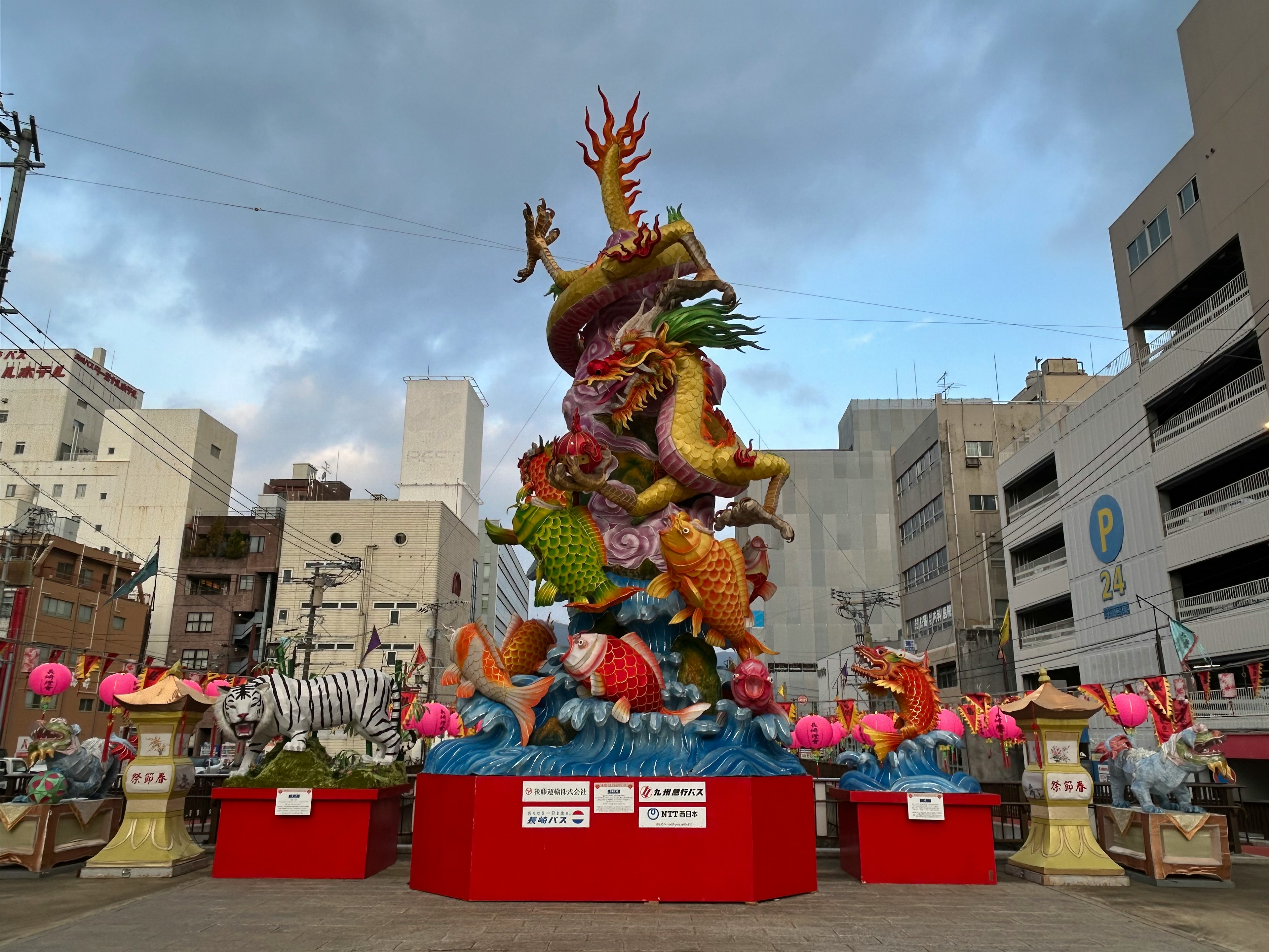 Une statue de dragon colorée se dresse dans une place avec des bâtiments en arrière-plan