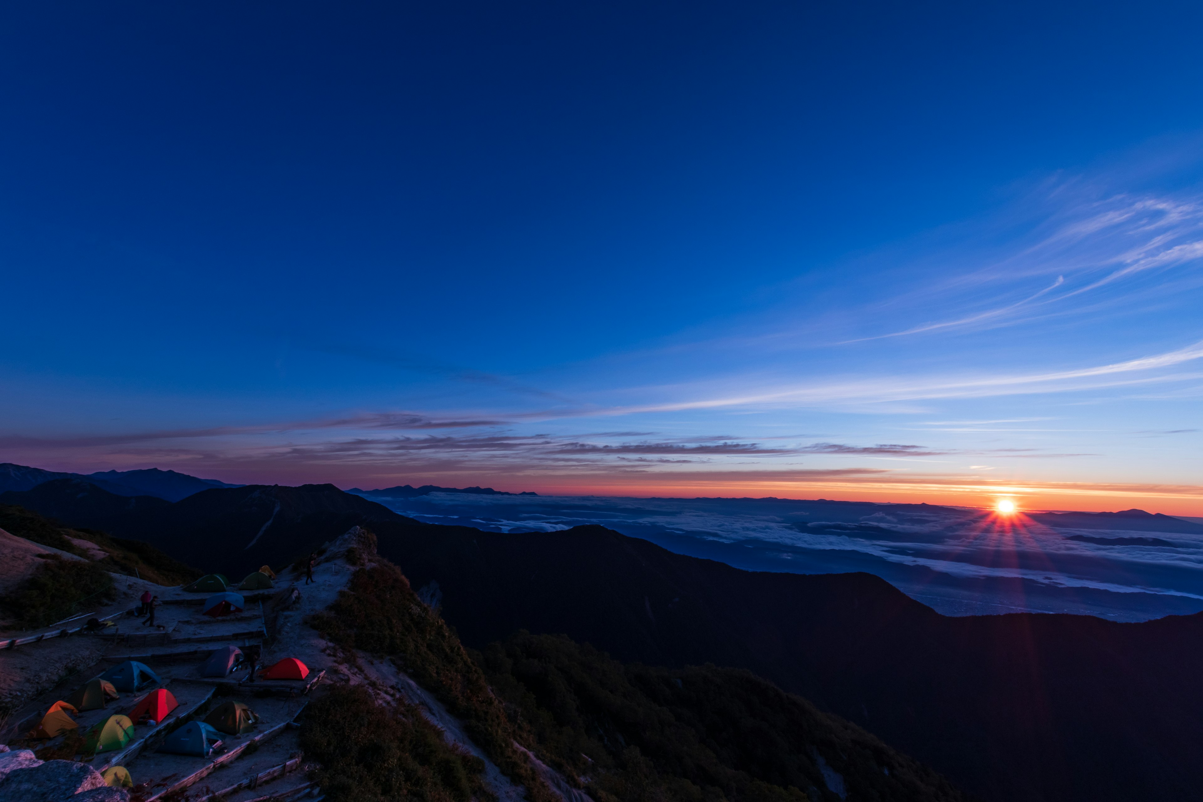 Pemandangan matahari terbenam yang menakjubkan di atas puncak gunung dengan tenda di latar depan