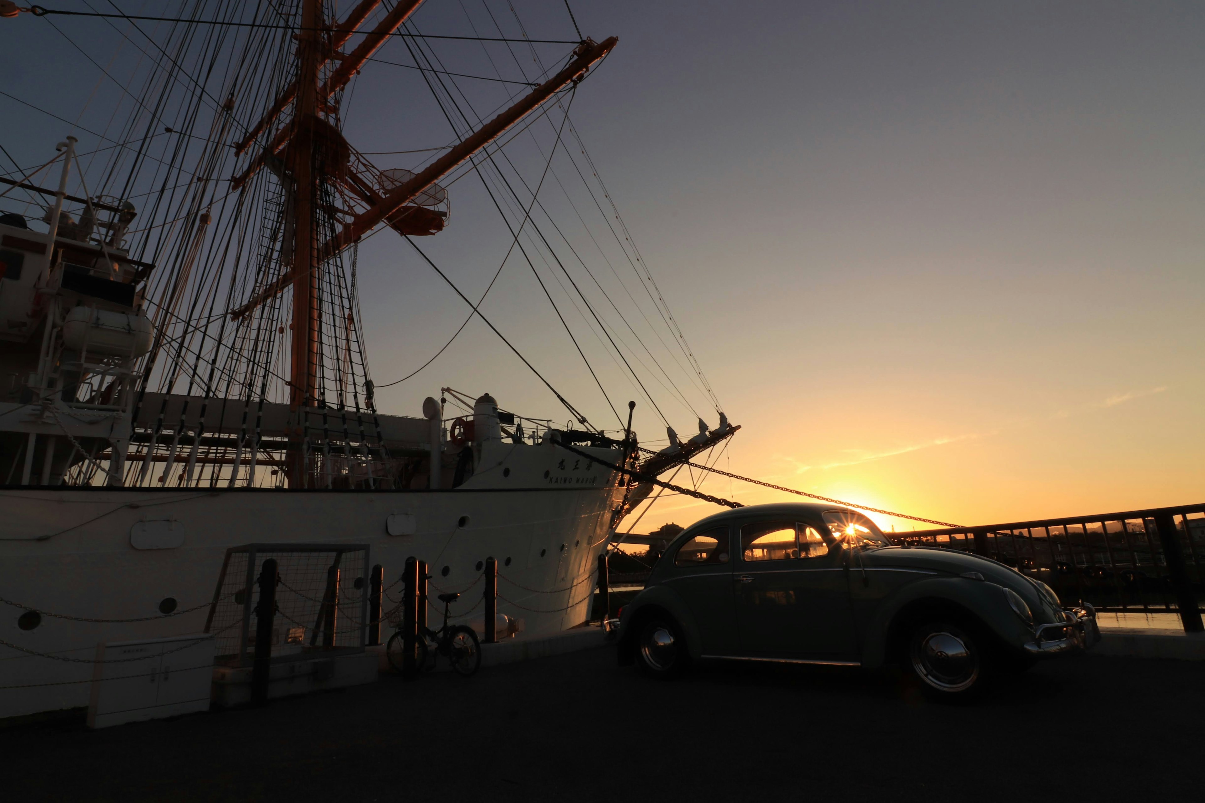 Silhouette of a ship and a Beetle car against a sunset