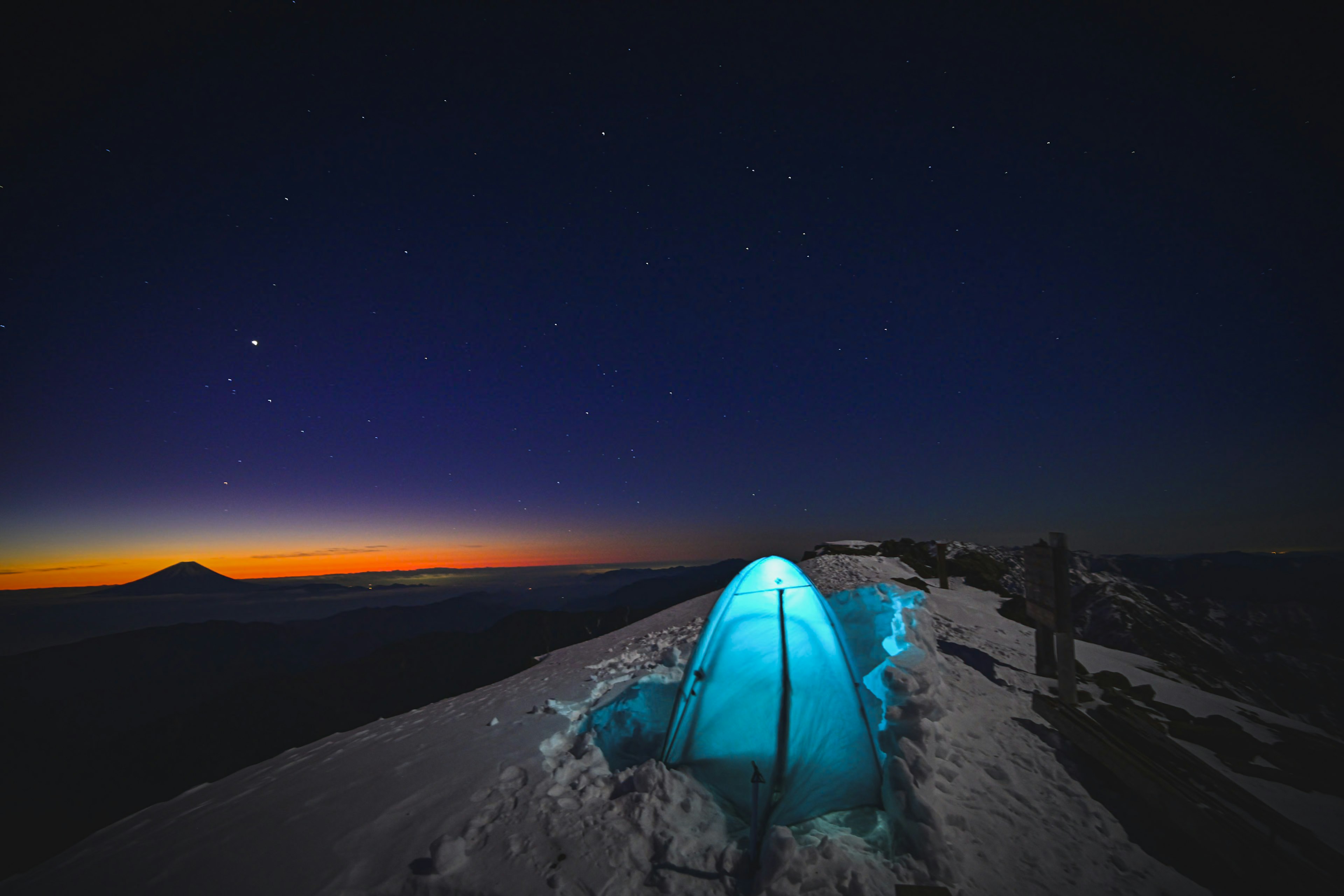 Una tienda azul en la nieve con un cielo estrellado y un amanecer en el fondo