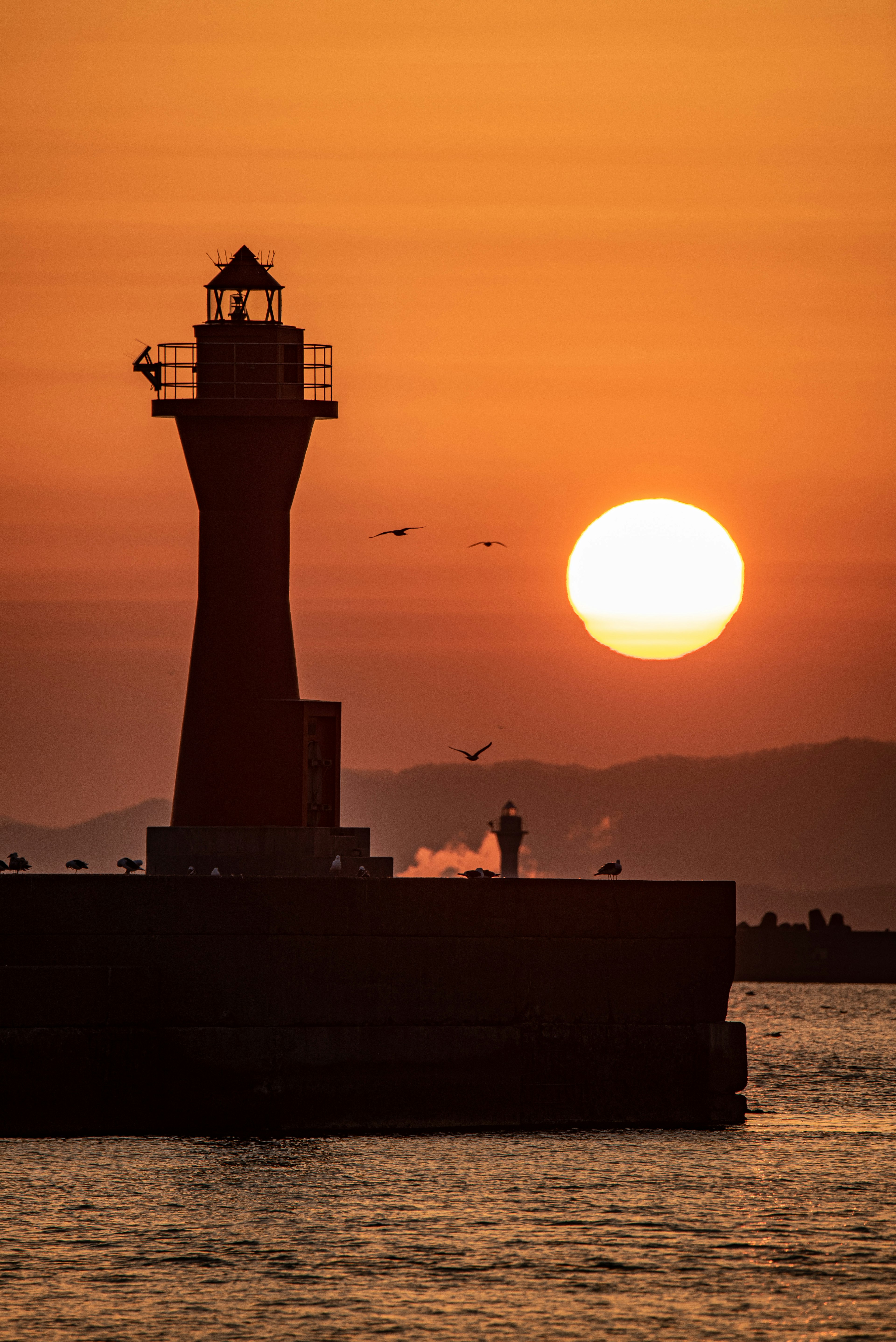 夕陽背景下的燈塔輪廓海洋景觀