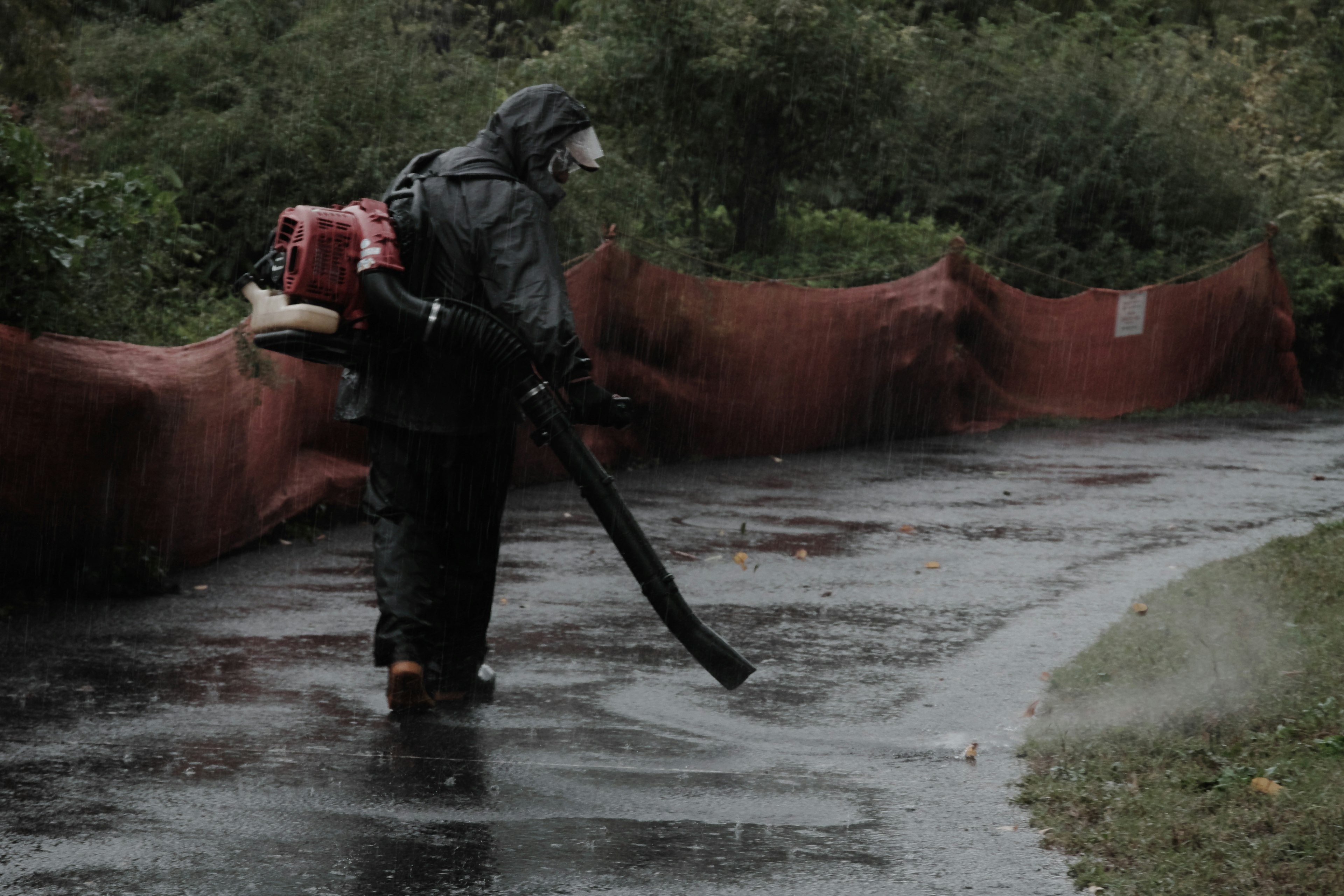 Trabajador usando un soplador de hojas en un camino mojado