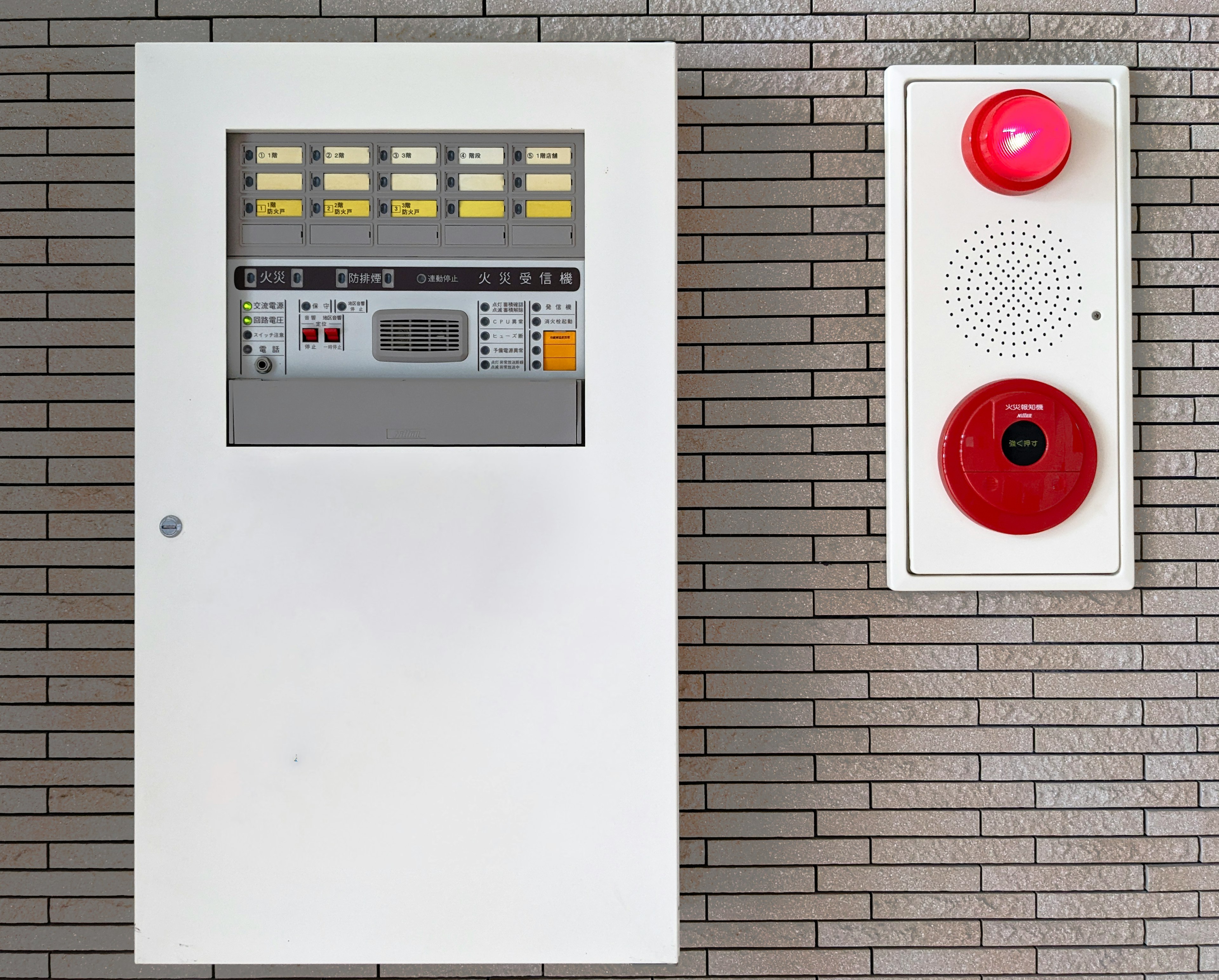 White fire alarm panel with buttons and a red alarm button mounted on a wall