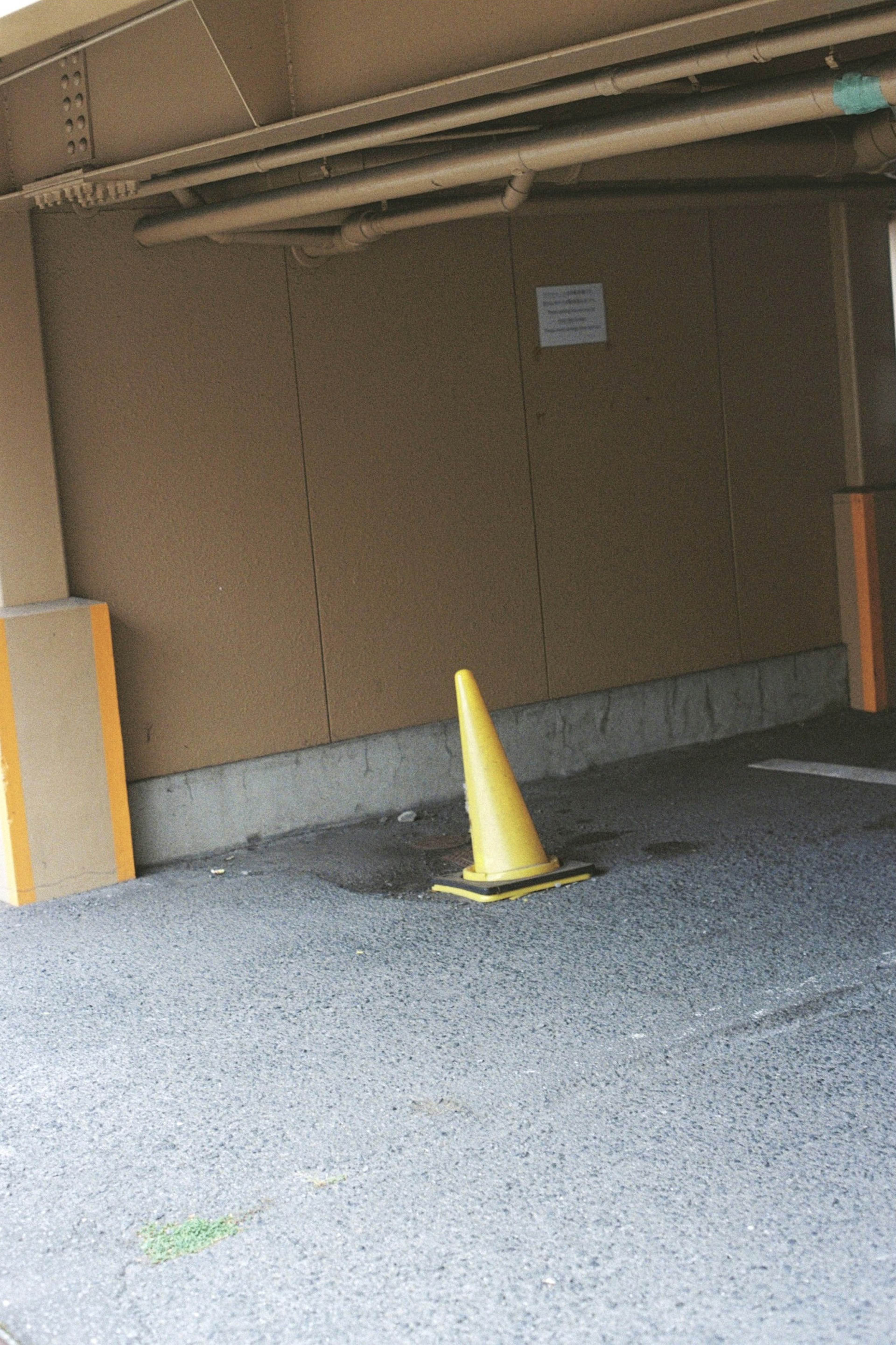 Yellow traffic cone placed in a parking area with a brown wall