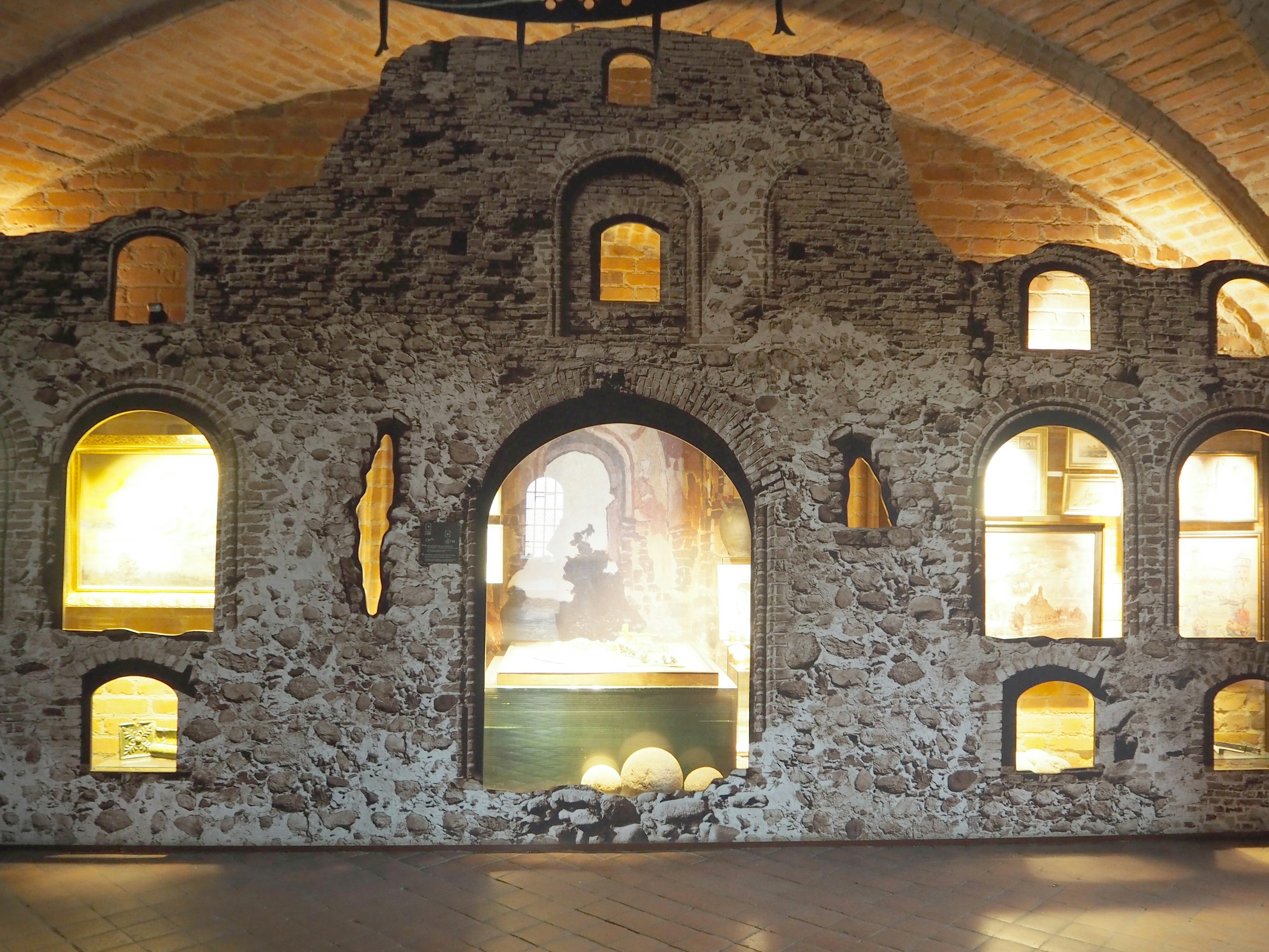 Photo of an interior space with an old stone wall featuring arched windows