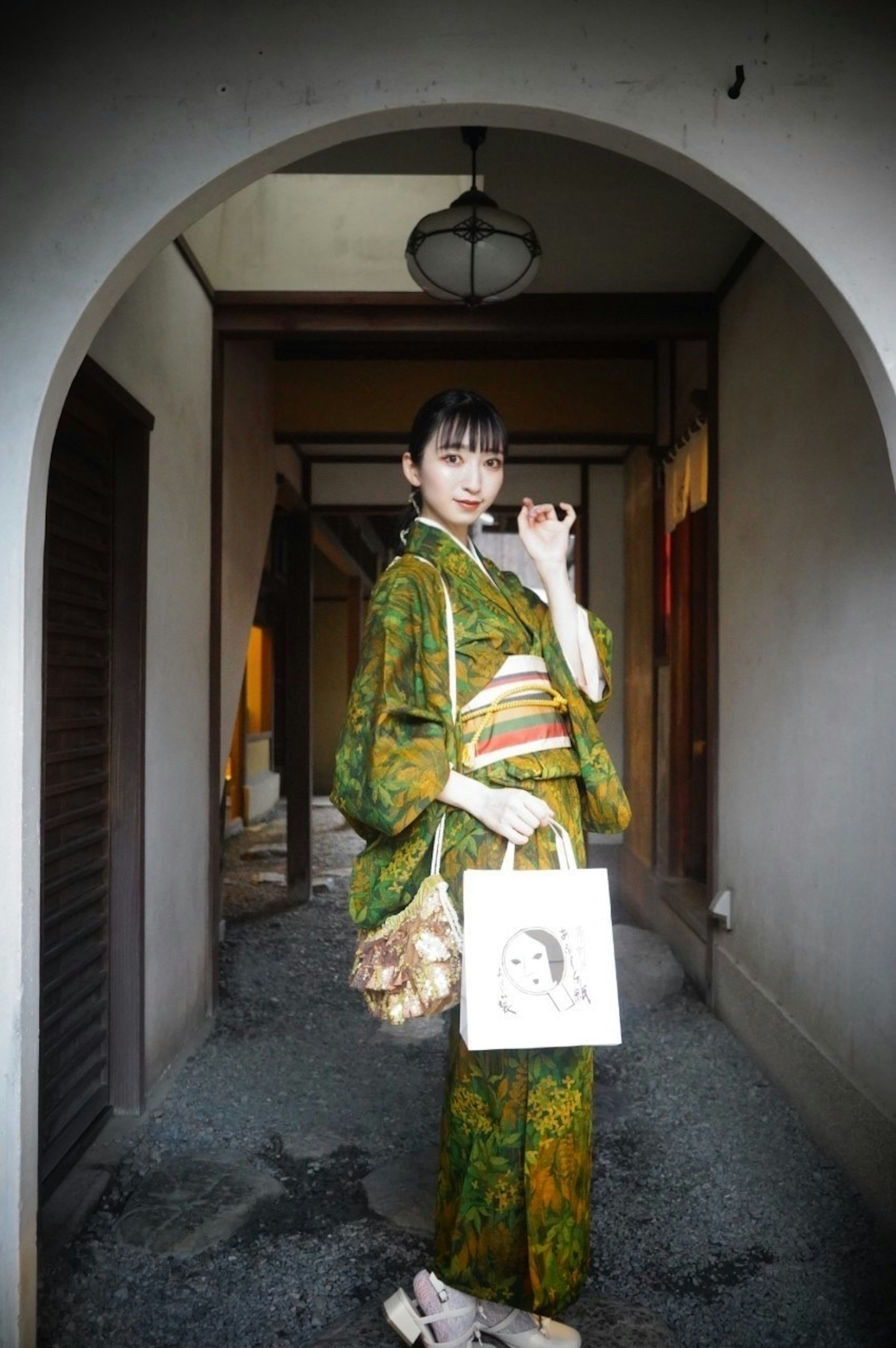 Una mujer en kimono verde está de pie en un arco