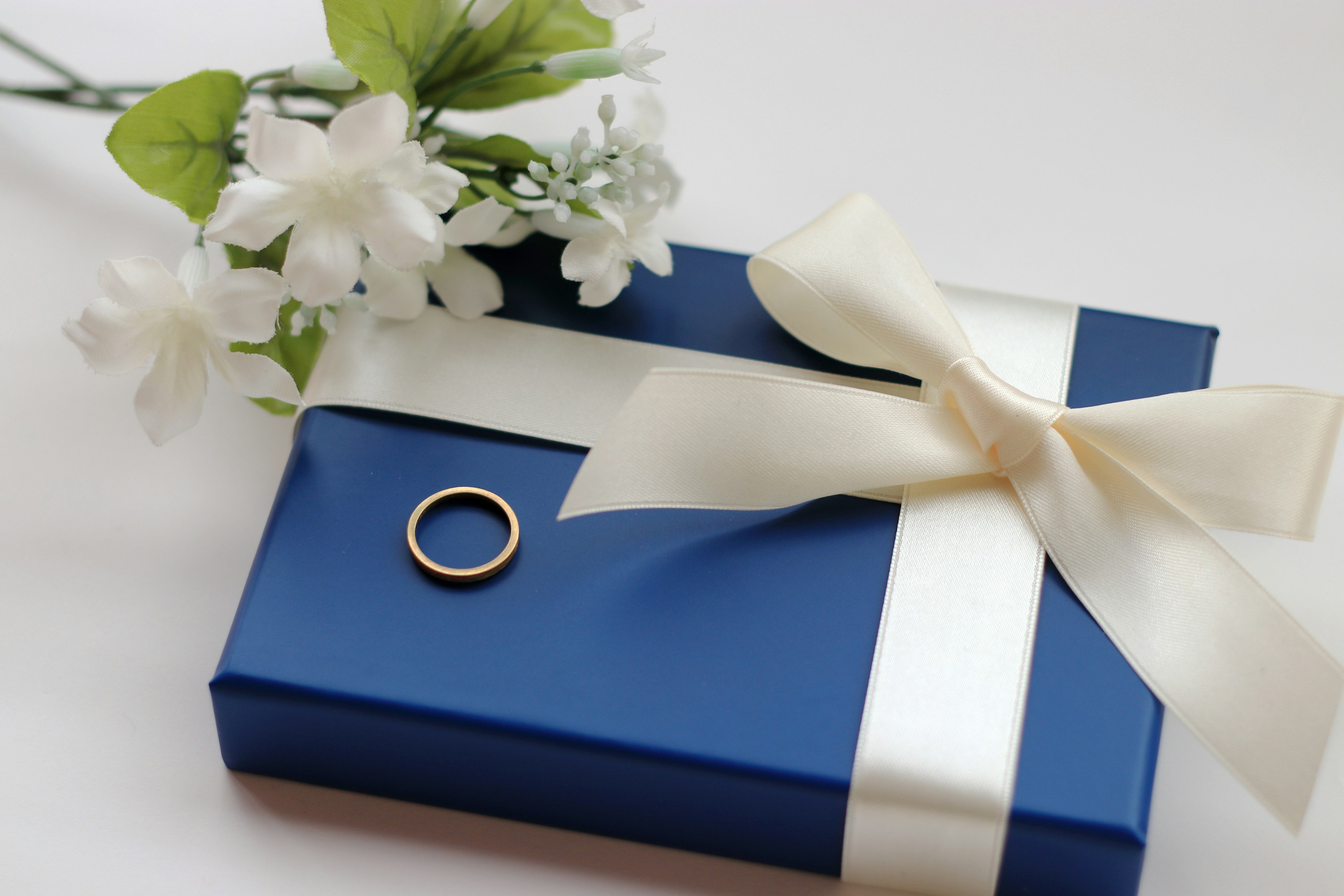 Caja de regalo azul con un lazo blanco que presenta un anillo y flores