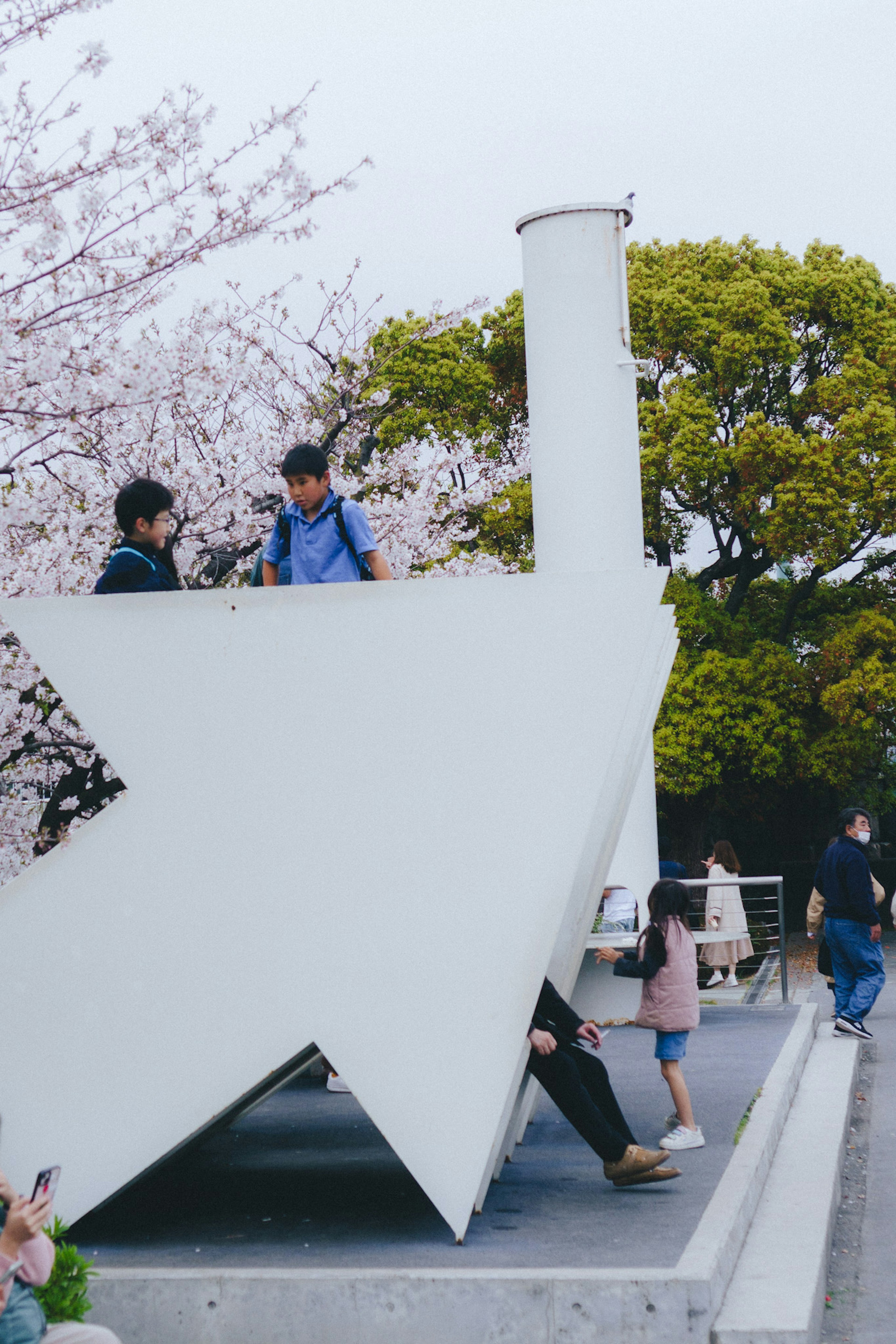 Enfants jouant sous des cerisiers en fleurs près d'une sculpture blanche