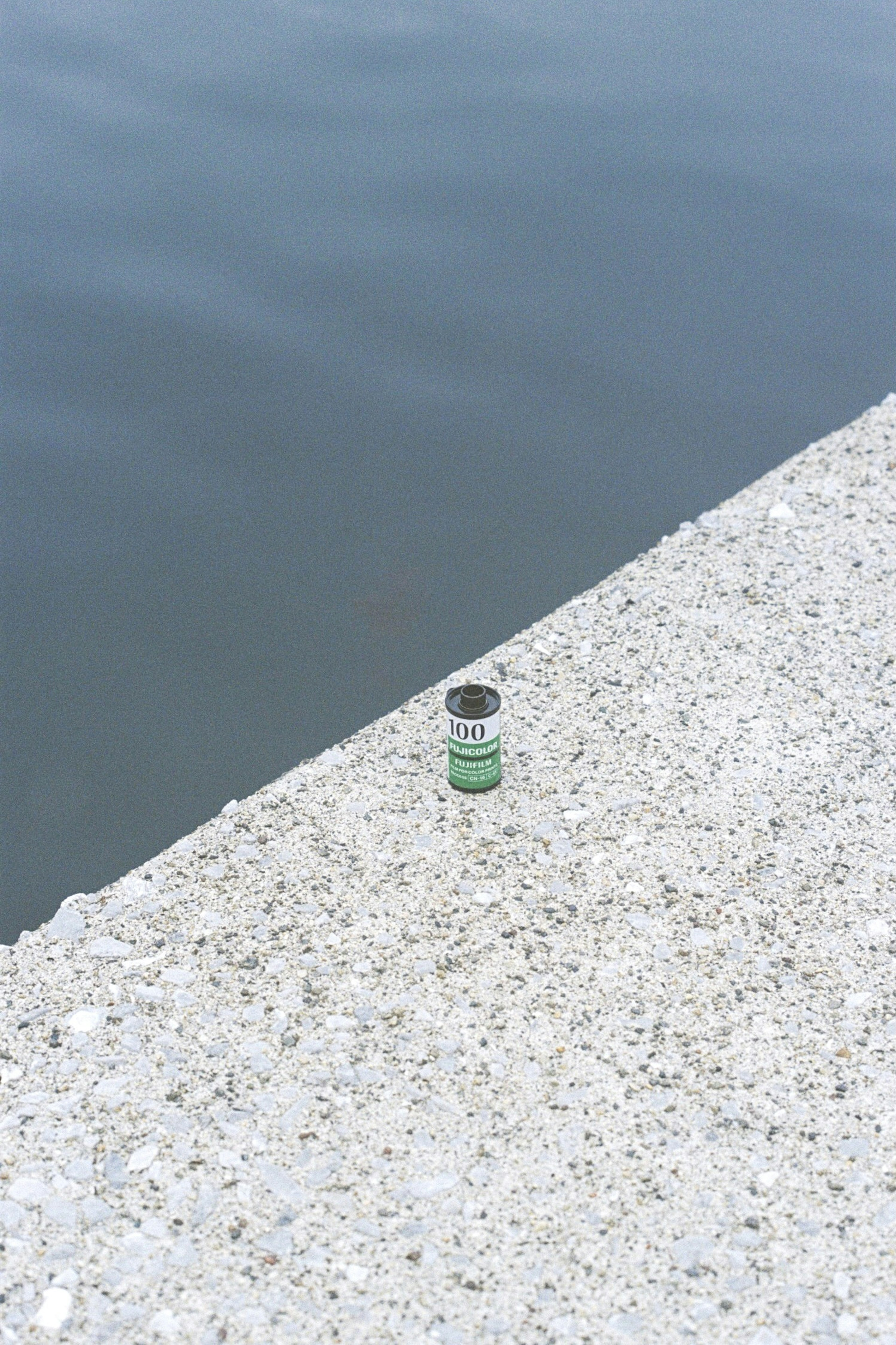 A green bottle placed on the concrete edge by the water