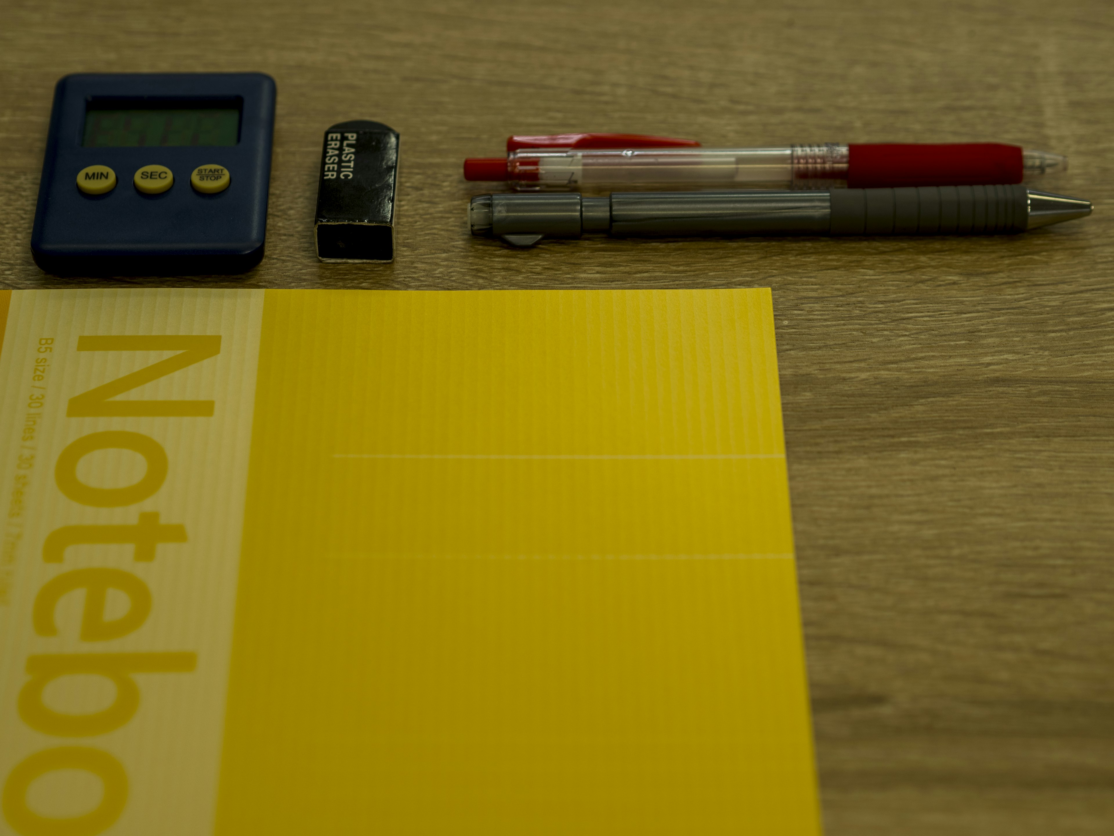 Image d'un carnet jaune avec des stylos, une calculatrice et une pile sur un bureau