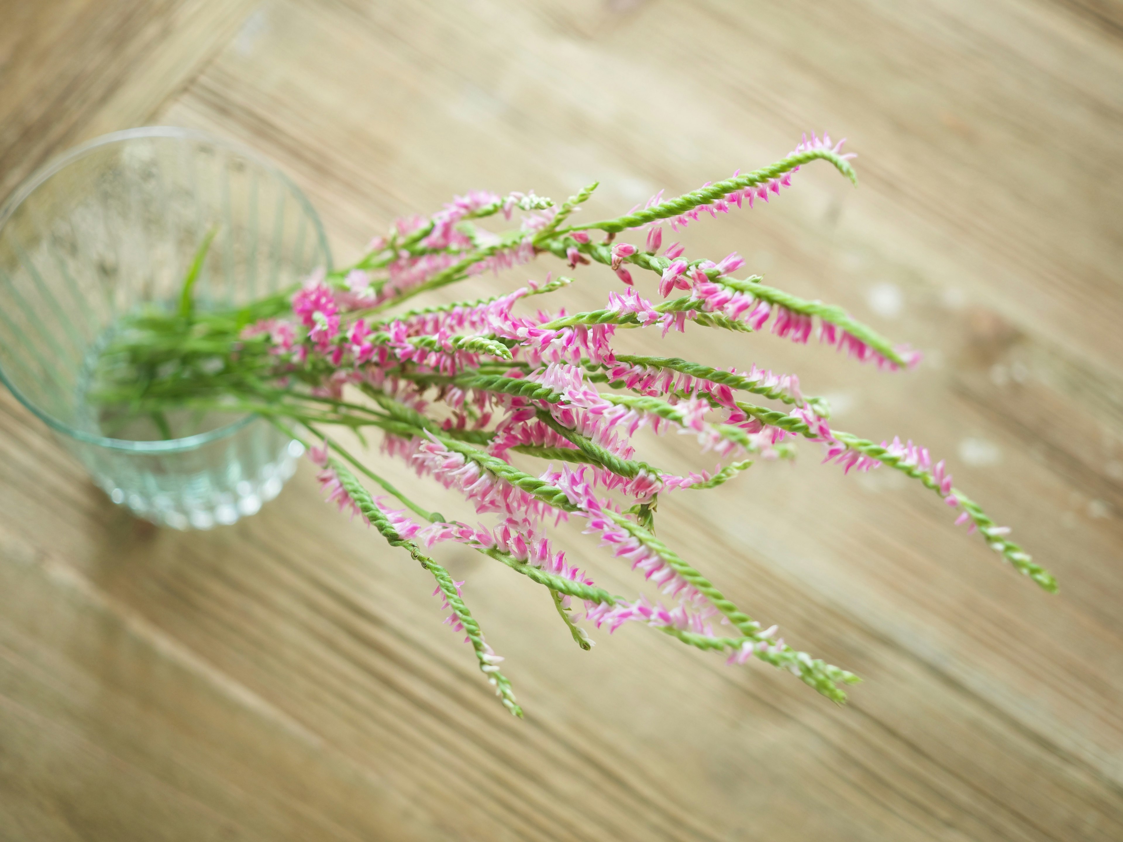 ピンクの花が入った透明な花瓶と木製のテーブル