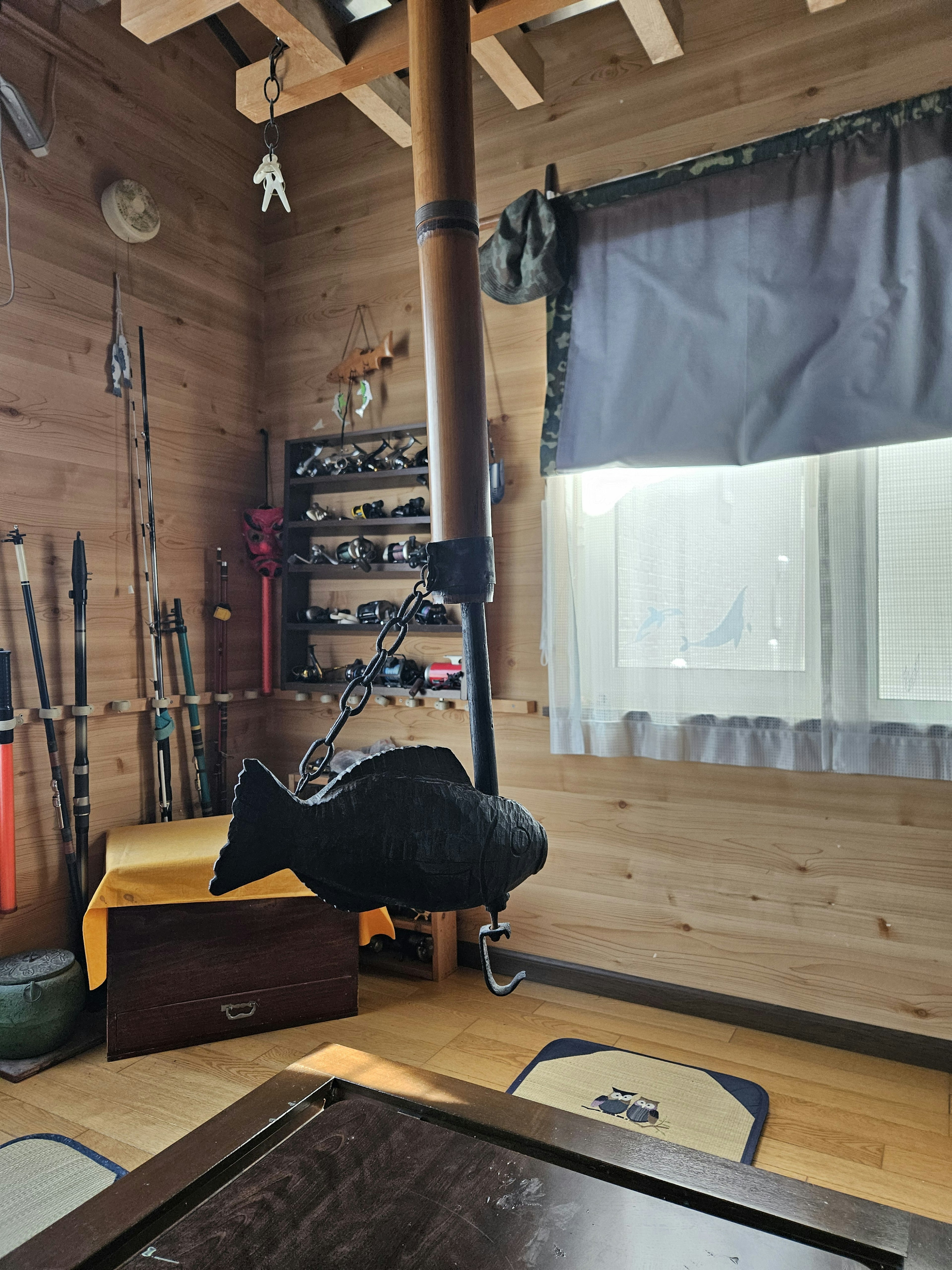 A black fish sculpture hanging in a wooden room with fishing gear displayed