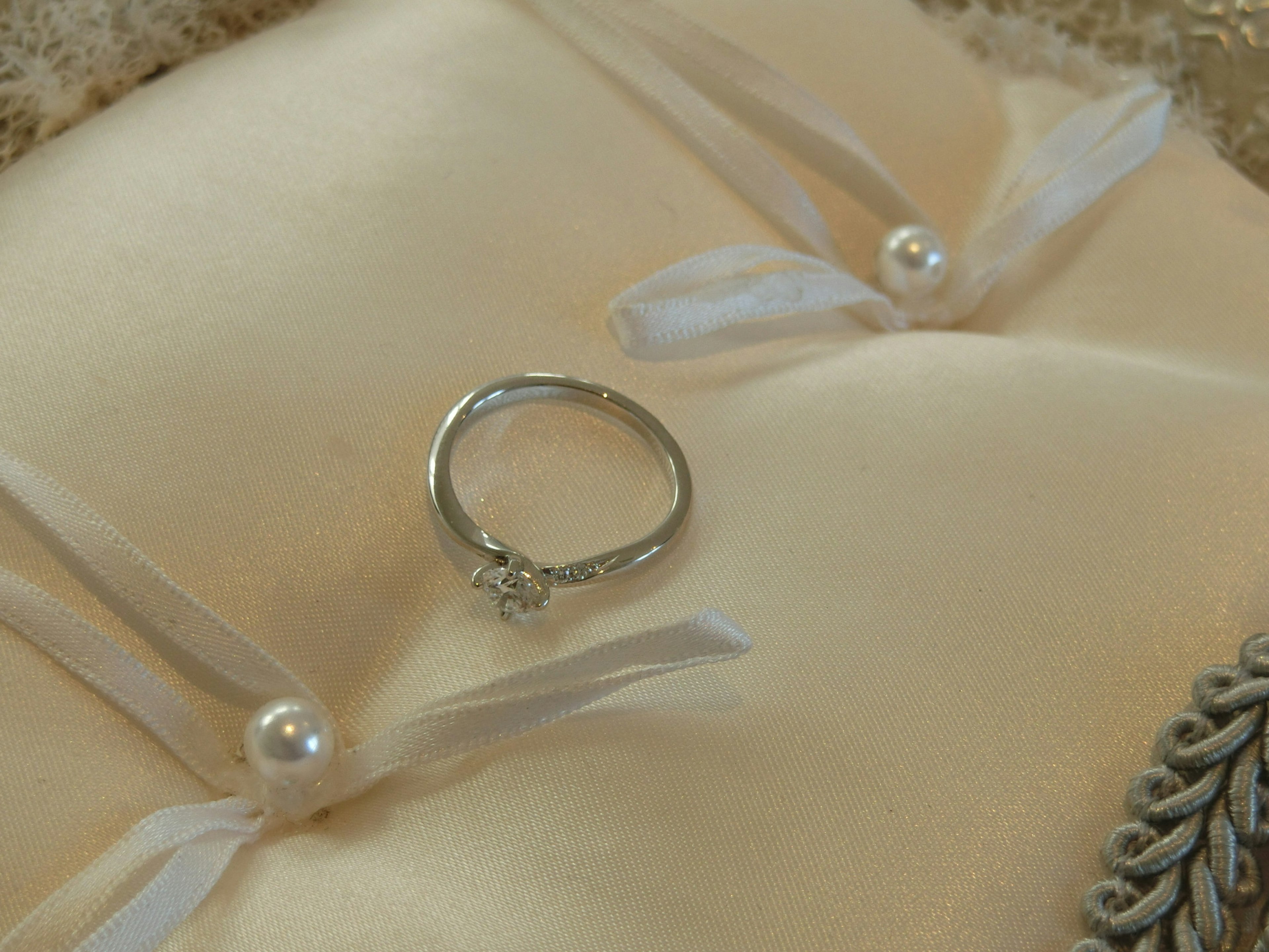 A silver ring placed on a cream-colored cushion adorned with pearl accents