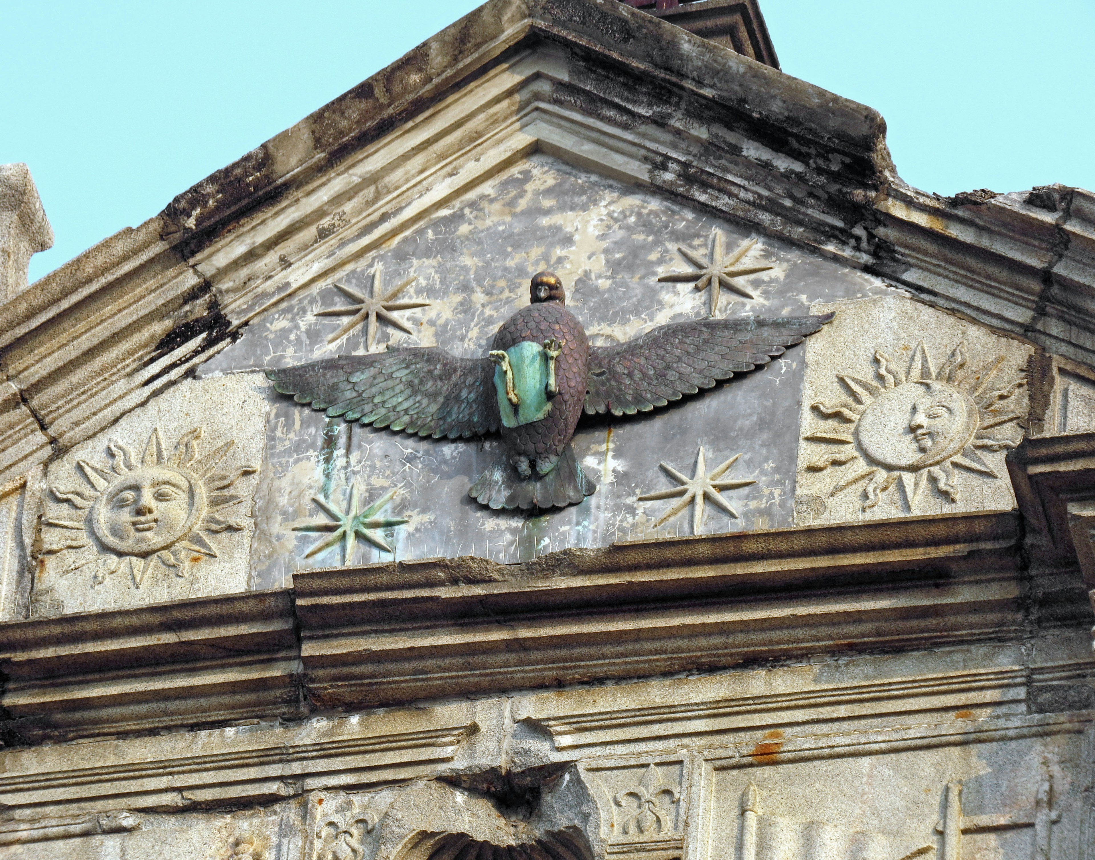 Eagle sculpture with outstretched wings on an old building roof featuring sun decorations