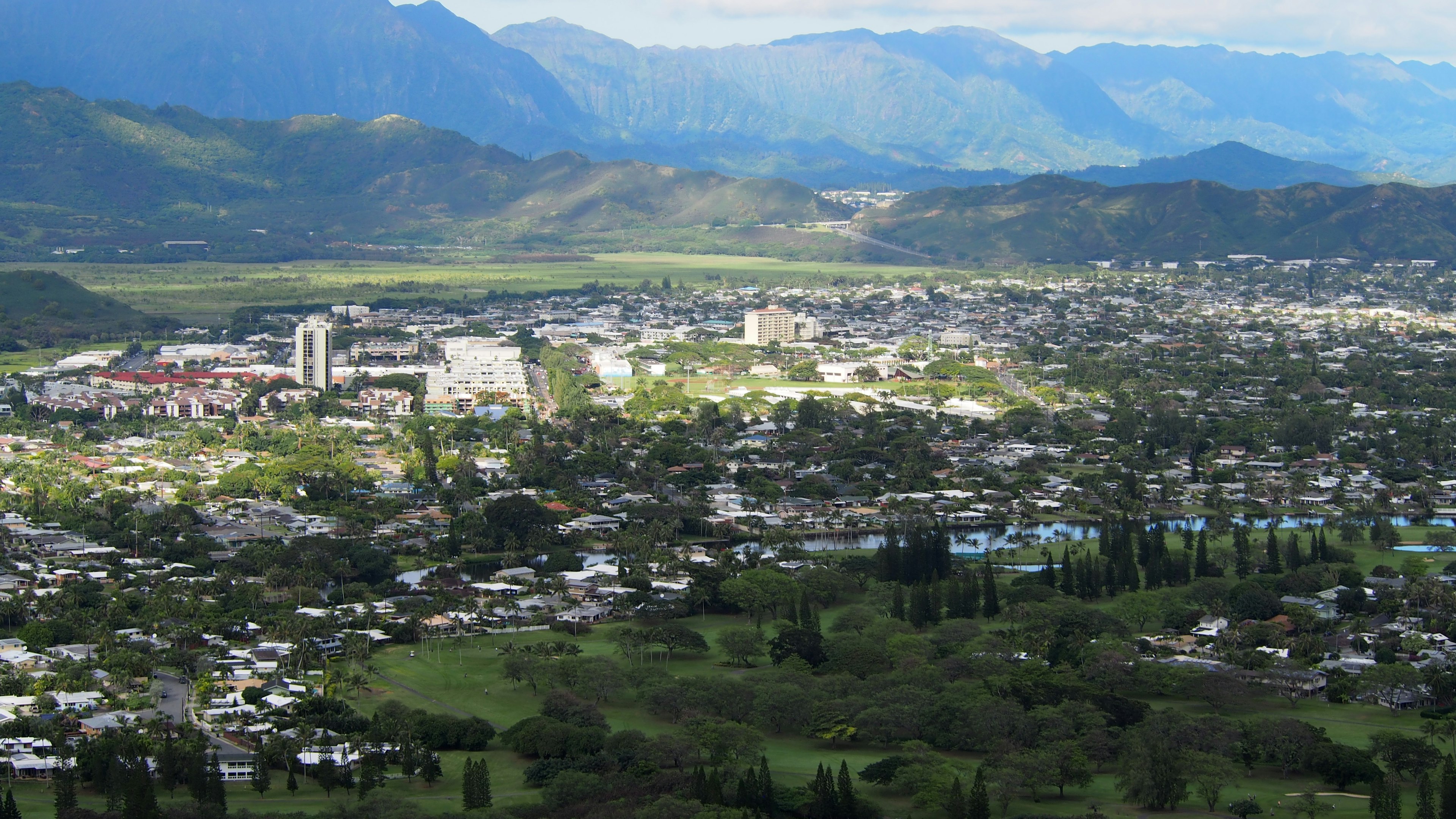 Un vaste paysage urbain entouré de montagnes avec des terrains verts et des bâtiments