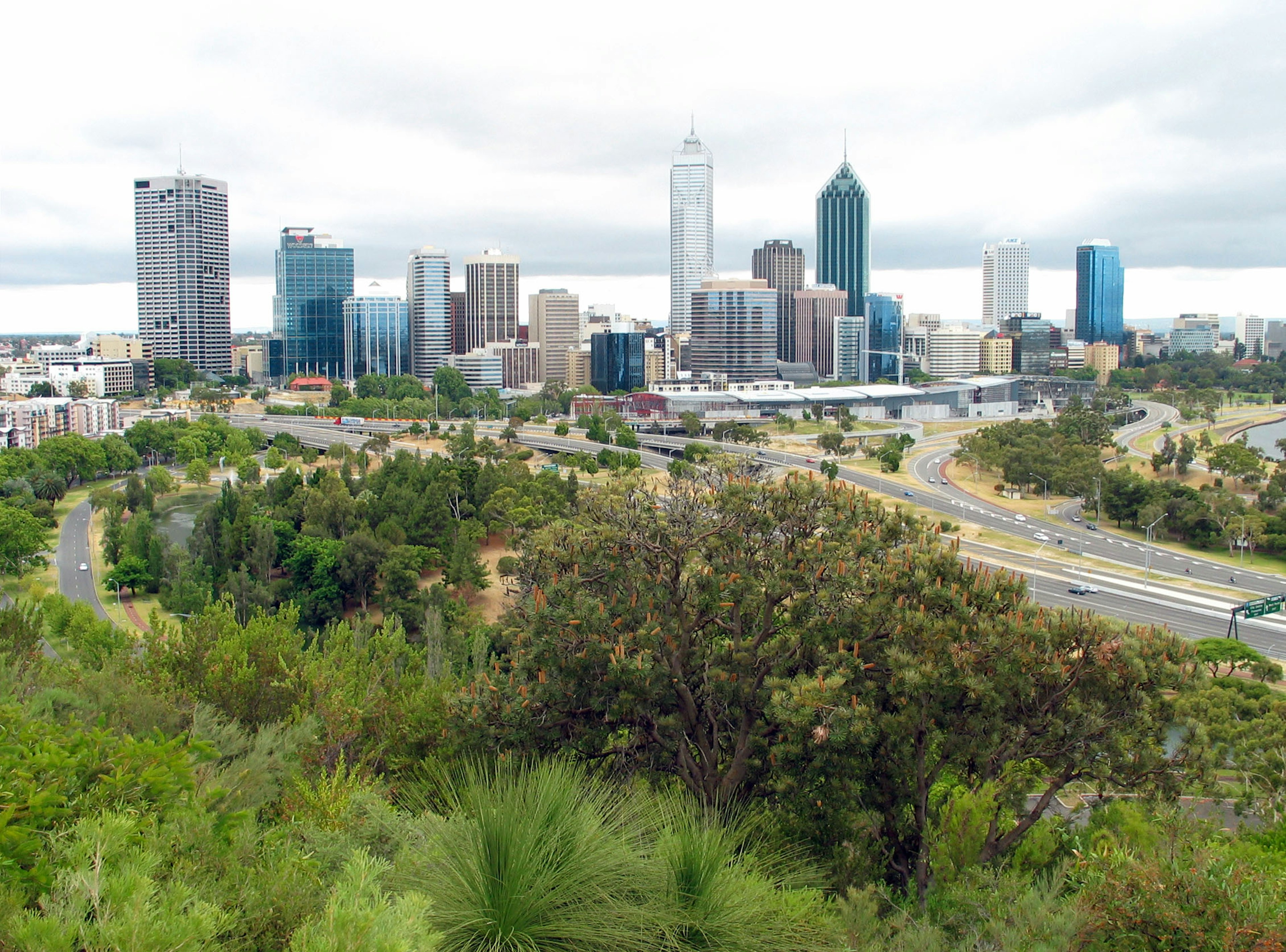 Skyline di Perth con grattacieli moderni e verde lussureggiante sotto un cielo nuvoloso