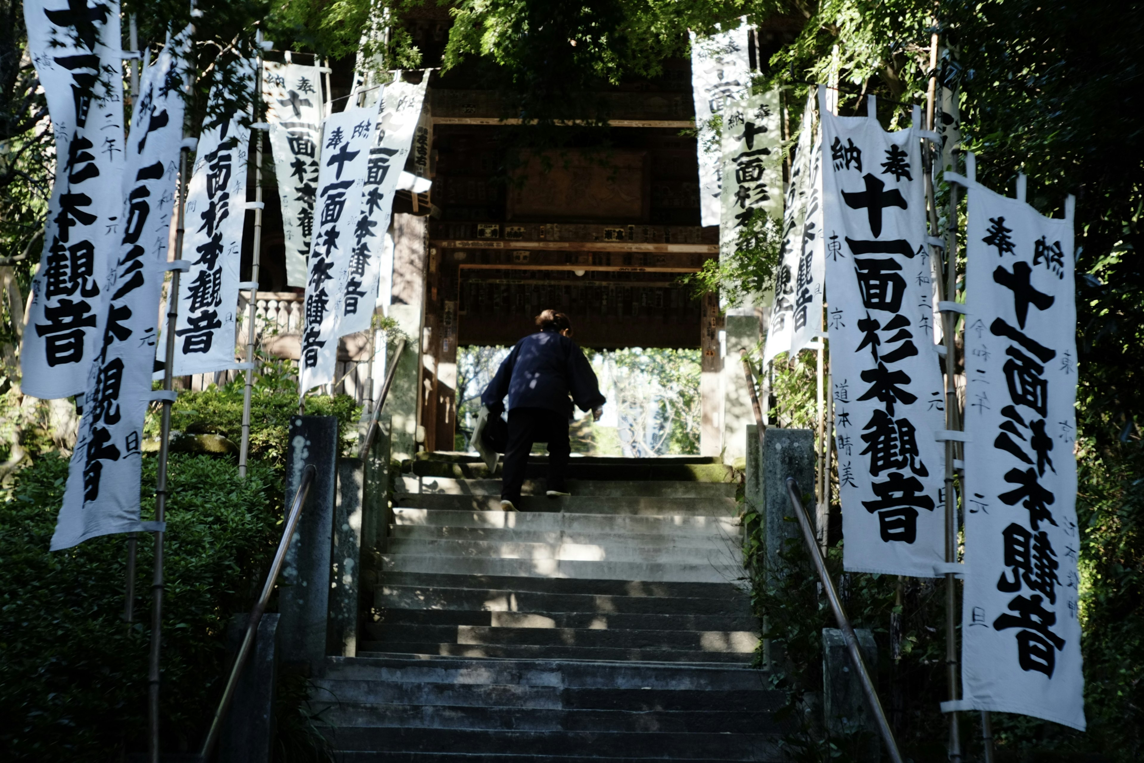 階段を上る人と周囲の白い旗が印象的な神社の風景