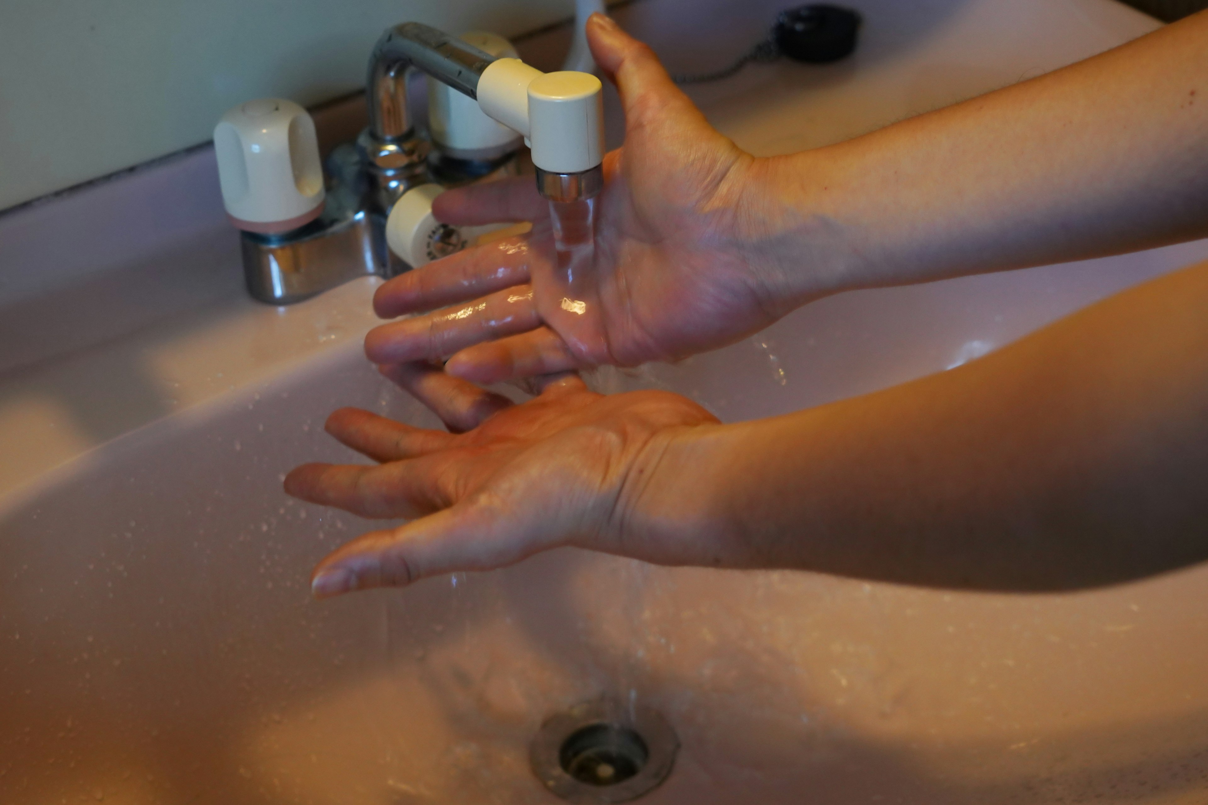 Persona lavándose las manos bajo el agua corriente en un lavabo rosa