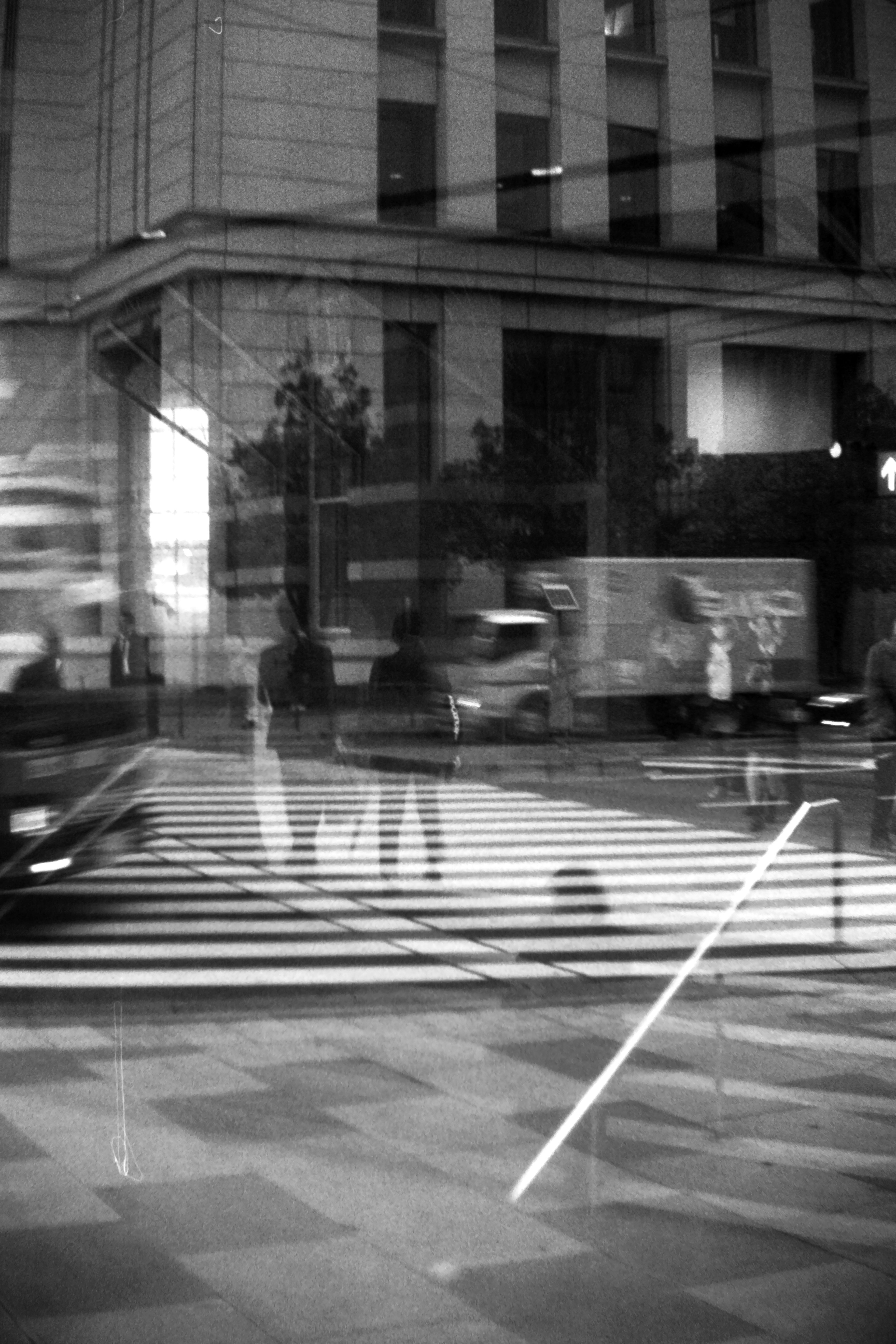 Escena urbana en blanco y negro con reflejos de personas en un paso de peatones