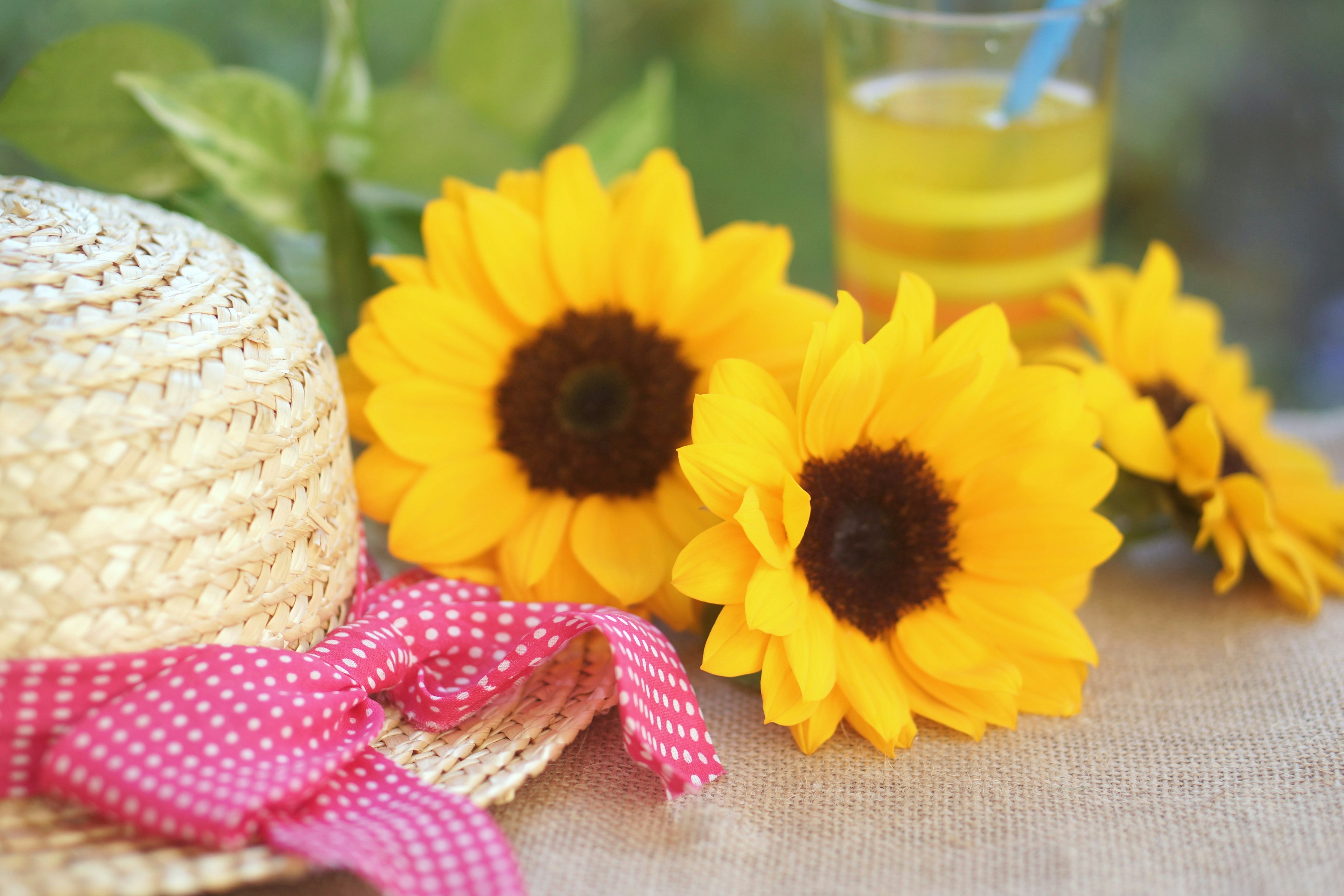 Straw hat and sunflowers arranged on a table with a refreshing drink