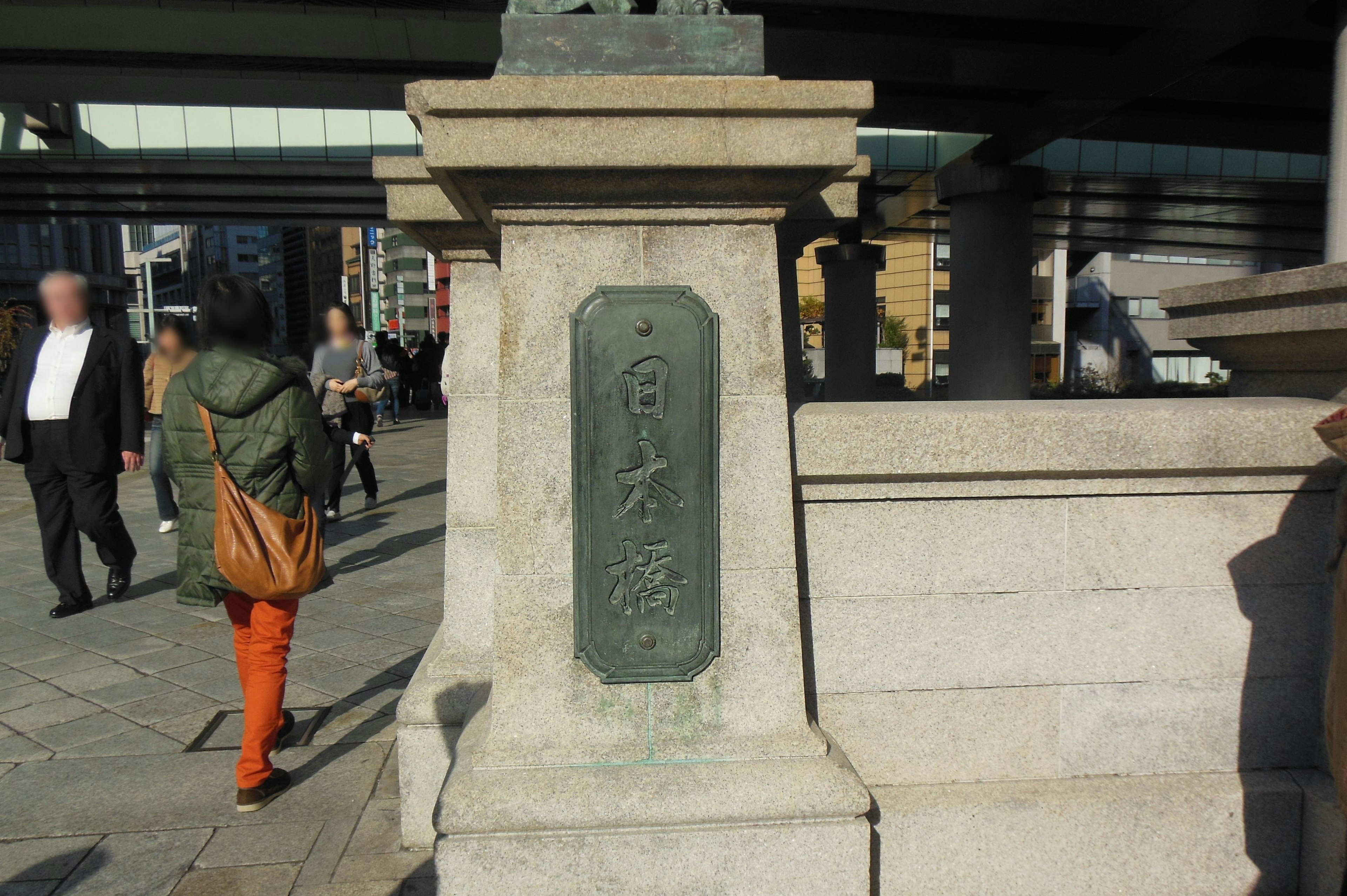 Steinsäule mit eingravierten Zeichen und umstehenden Passanten