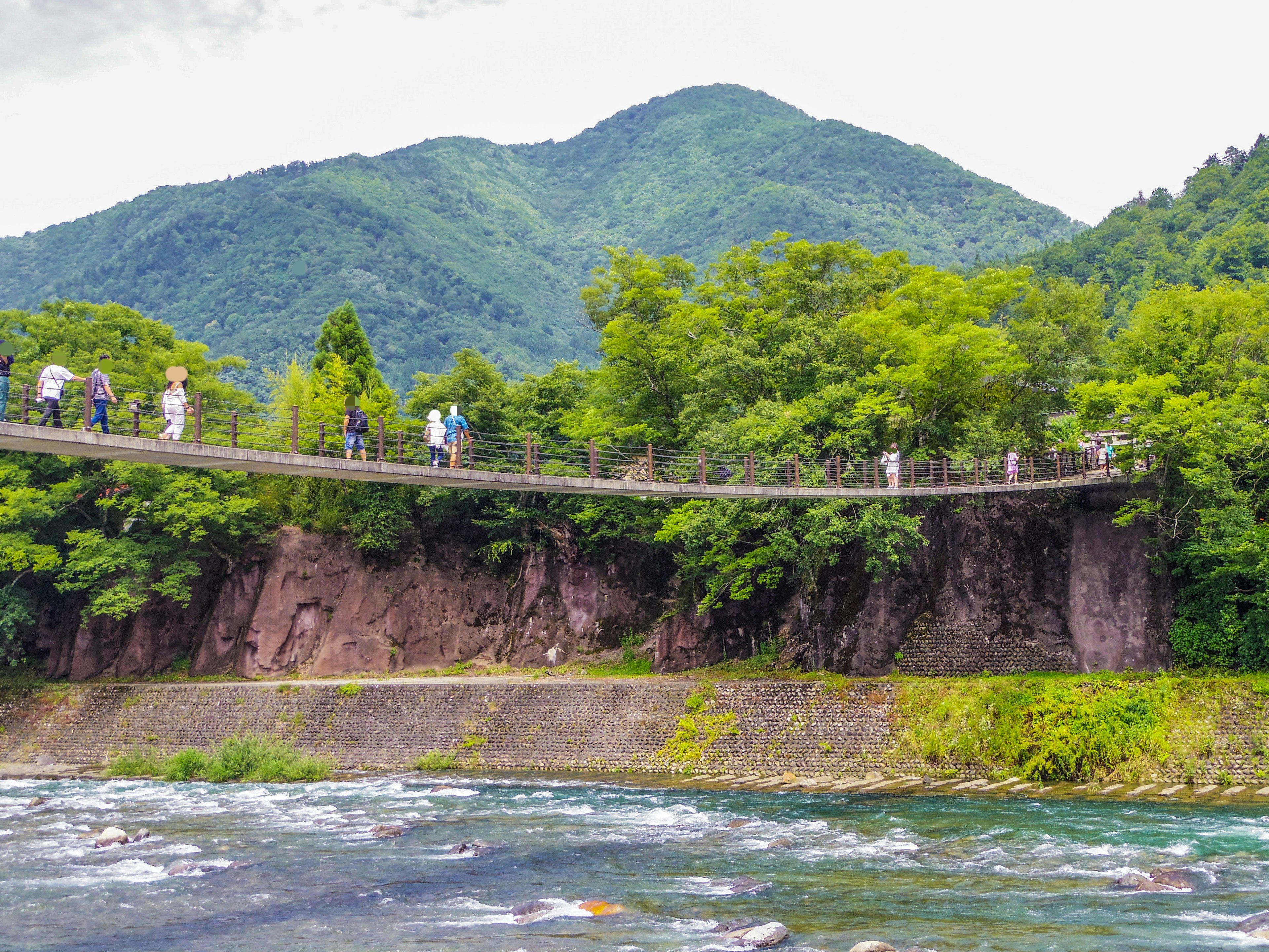 Des gens marchant sur un pont entouré de verdure avec de belles montagnes et une rivière