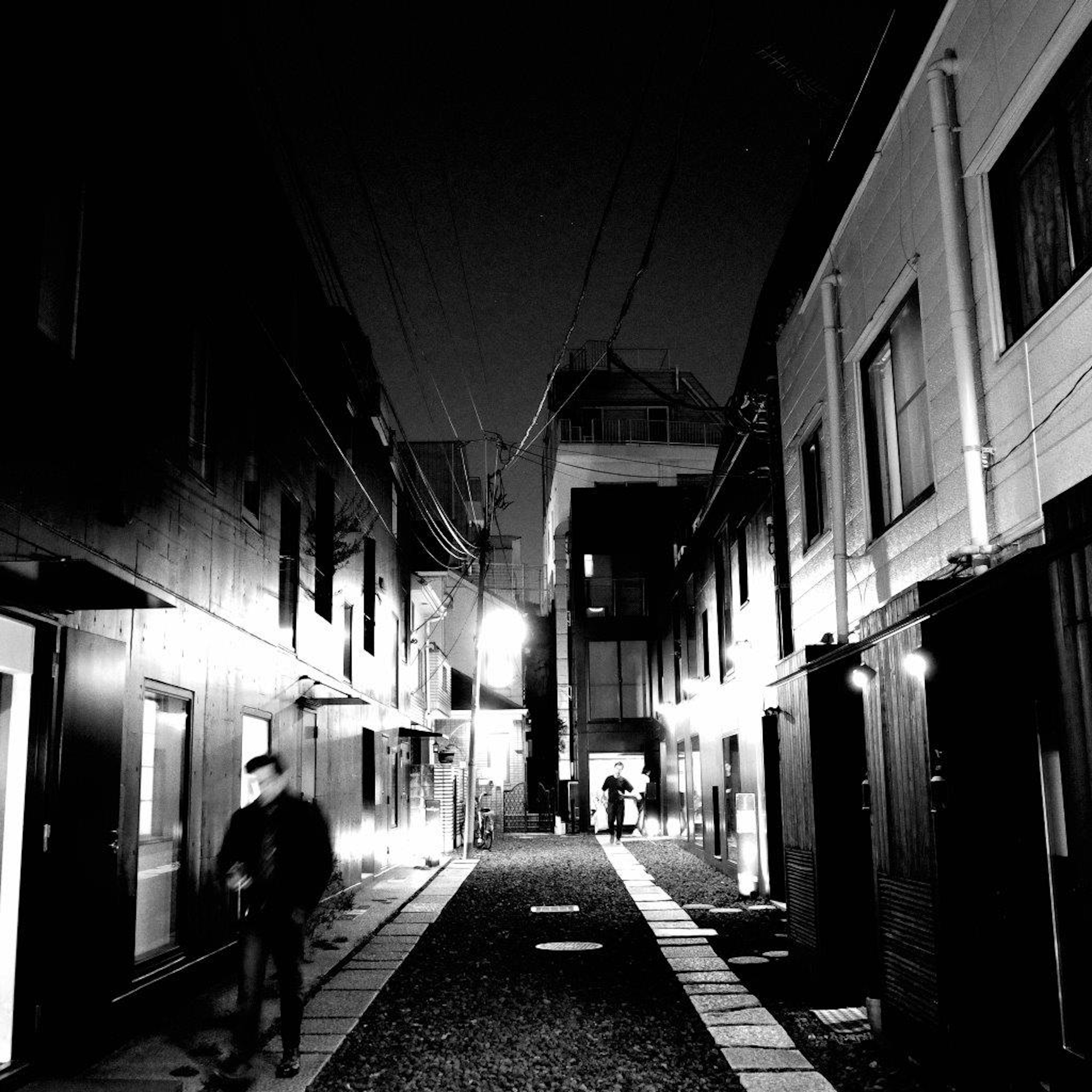 Photo en noir et blanc d'une ruelle calme la nuit avec une personne marchant