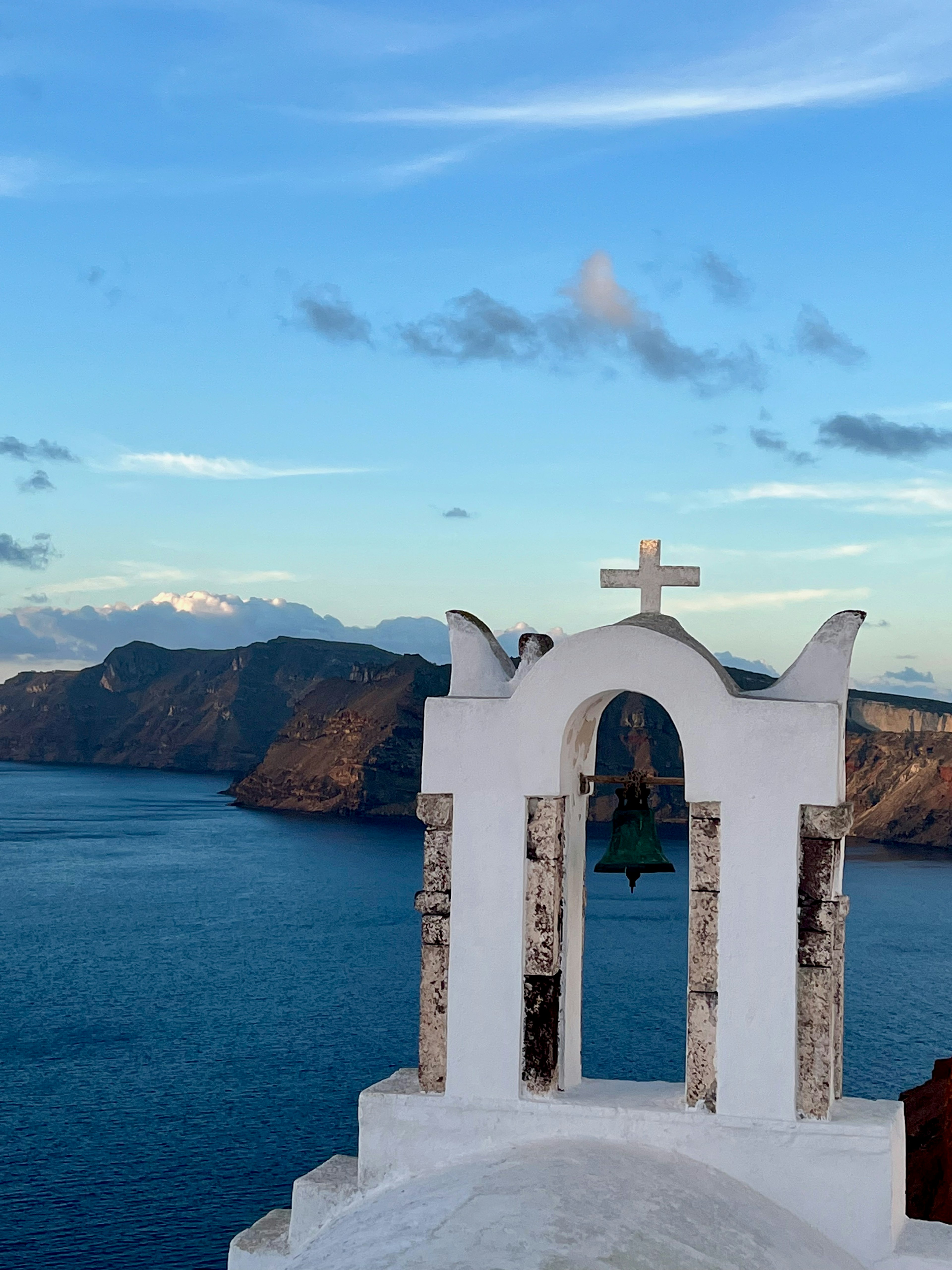 White church bell tower with a cross overlooking a beautiful sea view