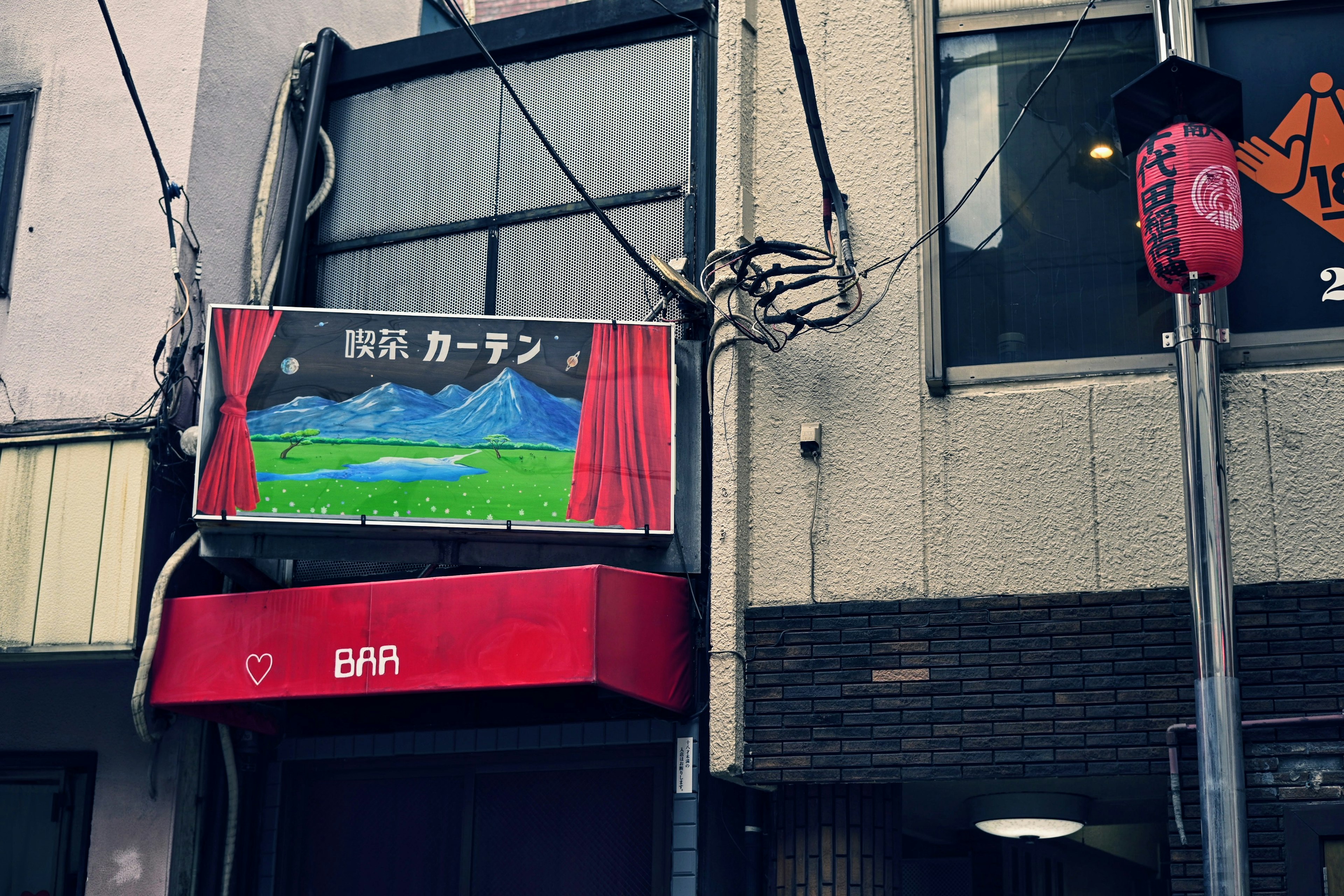 Exterior de una tienda con un letrero rojo y una pintura de paisaje