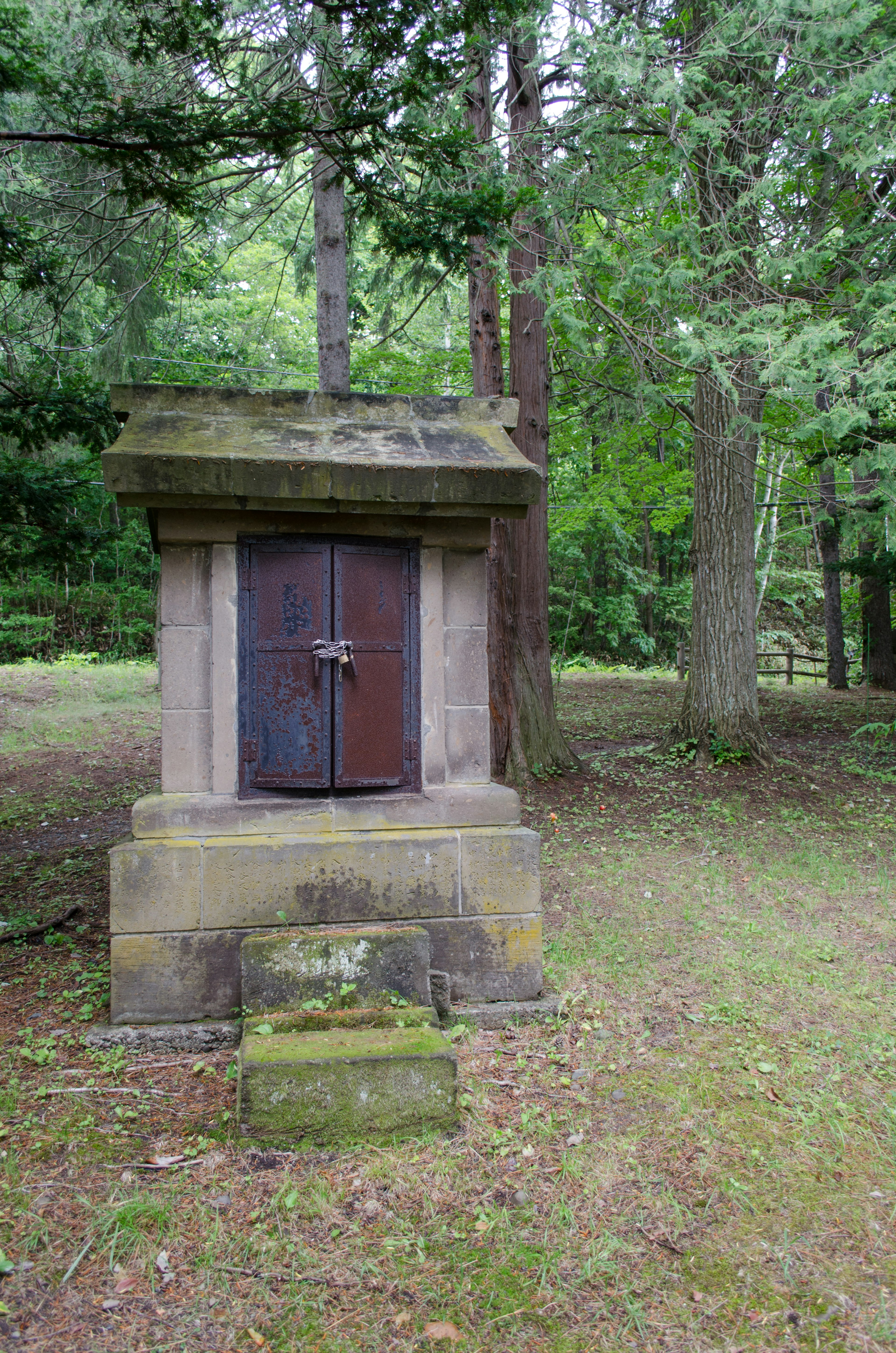 Una antigua estructura de piedra con una puerta oxidada en un bosque