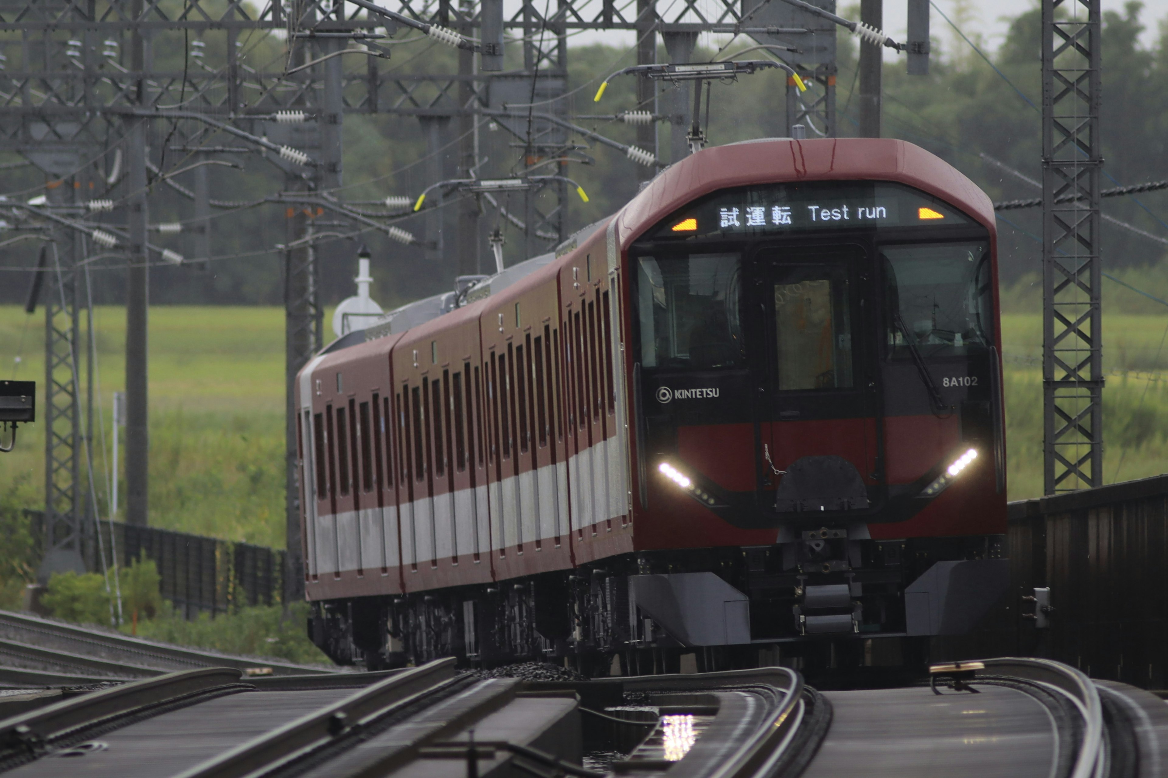 Red train traveling on tracks with green fields in the background