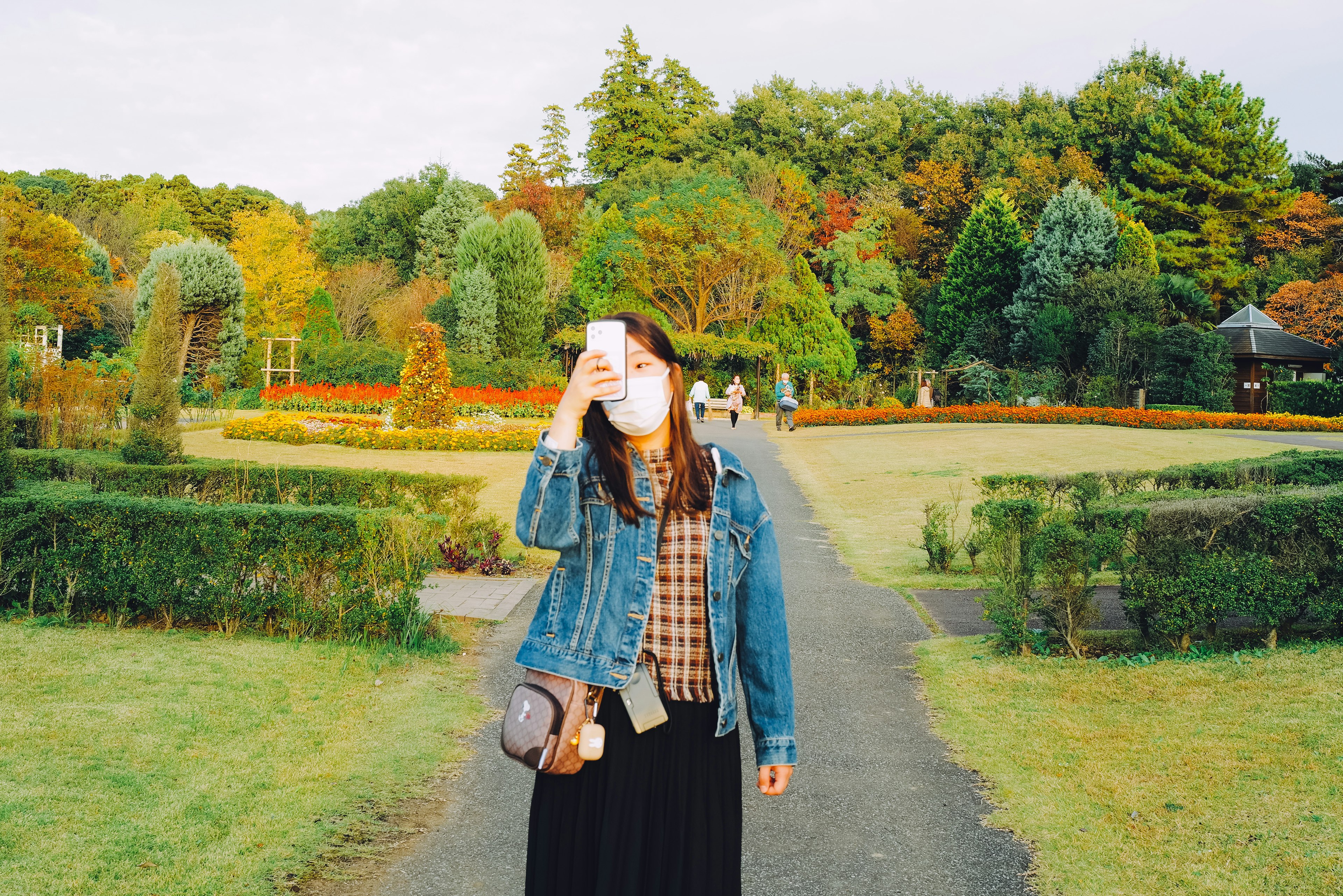 Una donna che tiene uno smartphone in un parco con abbigliamento casual e paesaggio autunnale