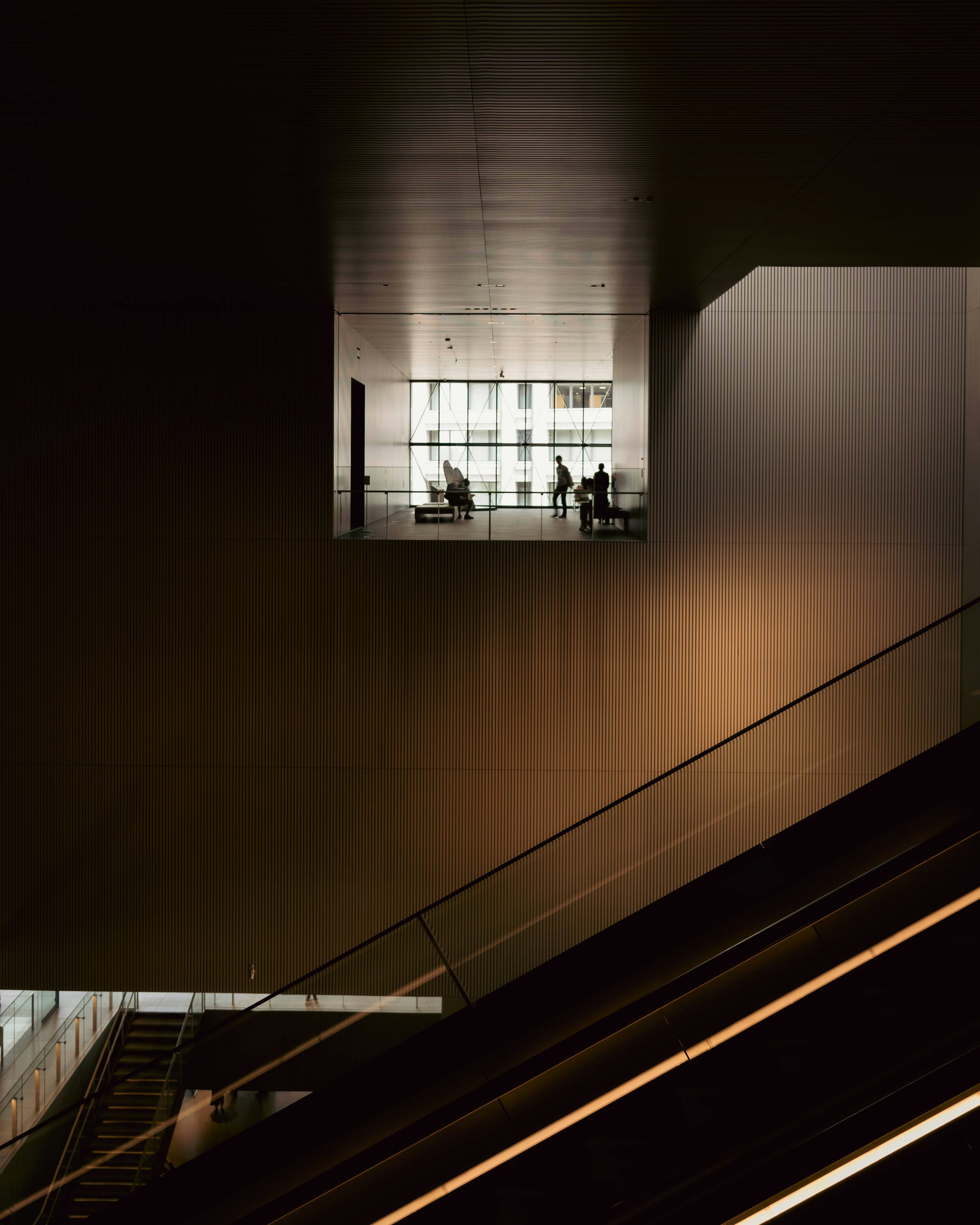 Interno di un edificio moderno con finestra luminosa e silhouettes di persone su sfondo scuro