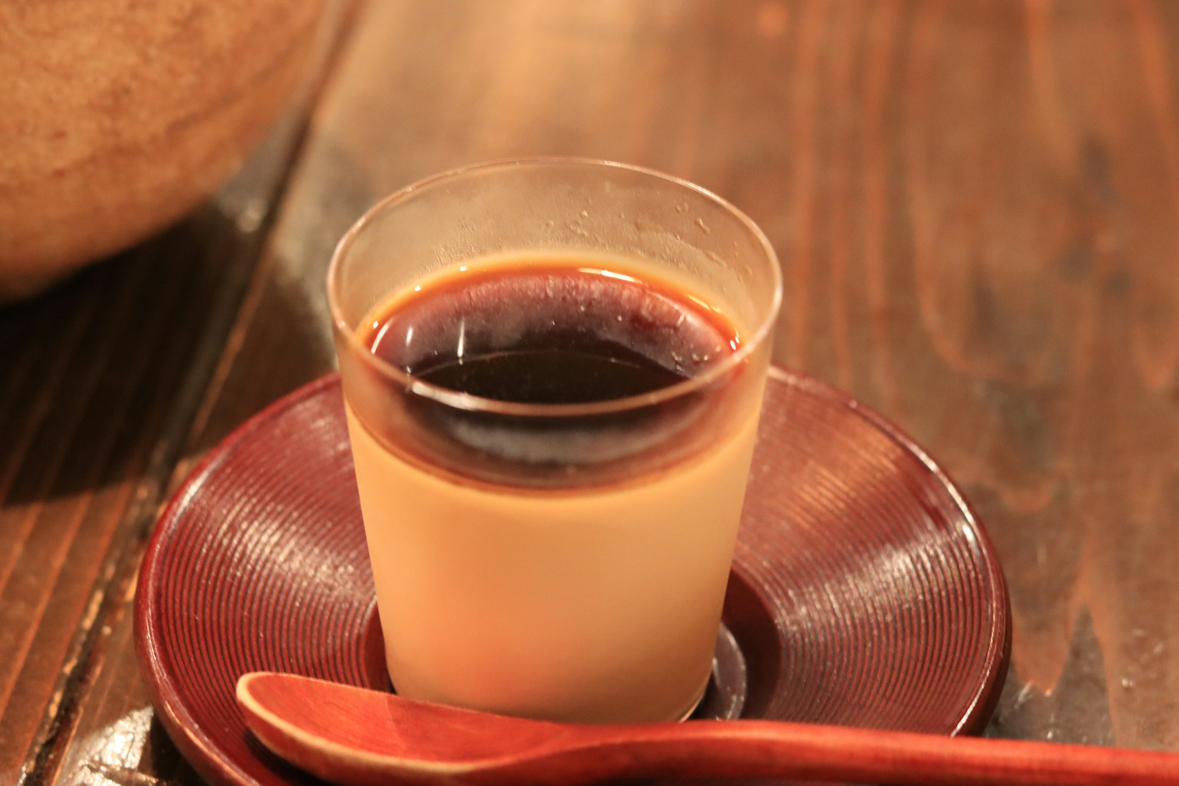 A glass cup with layered coffee and cream placed on a wooden table