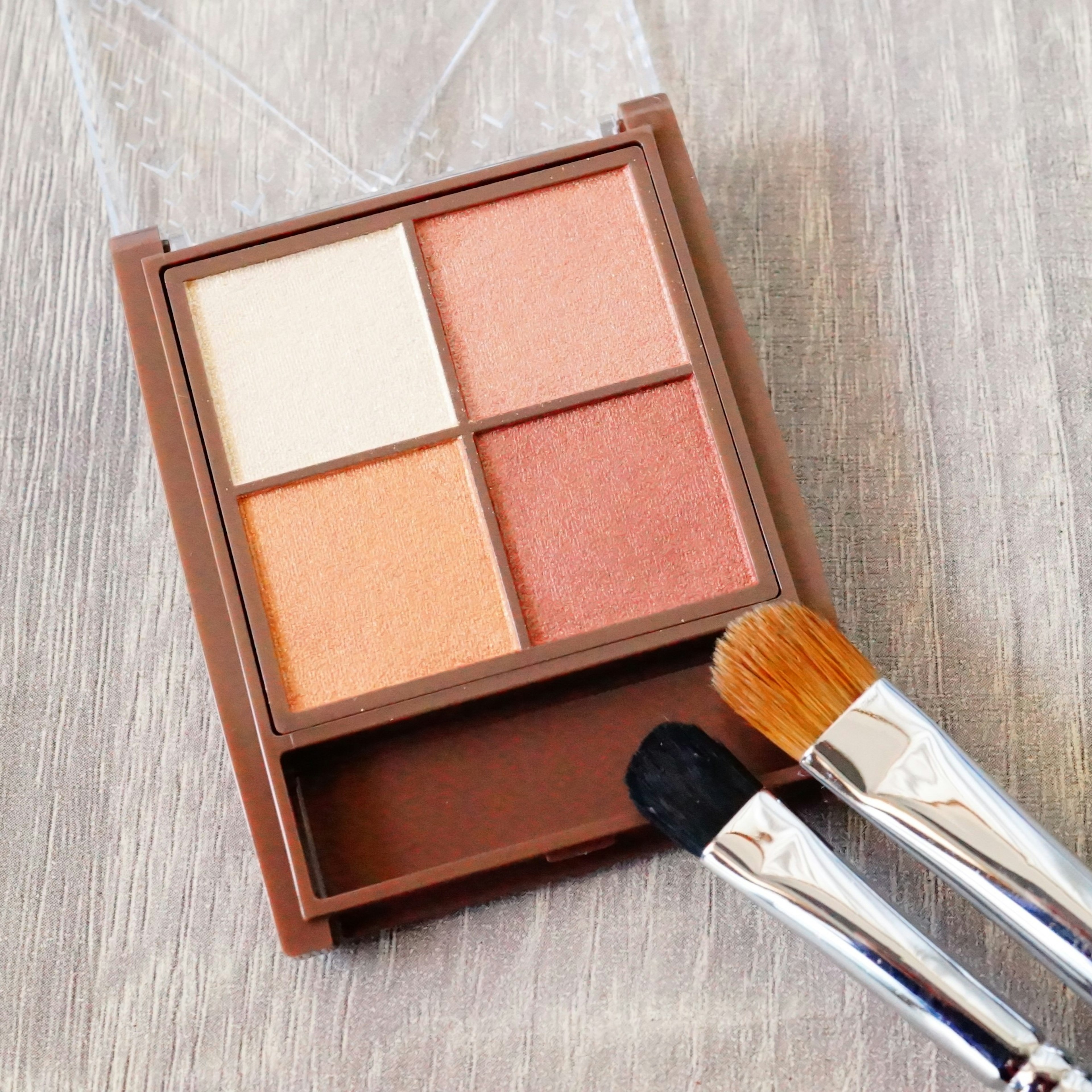 Palet coklat yang berisi empat warna eyeshadow dengan dua kuas di samping